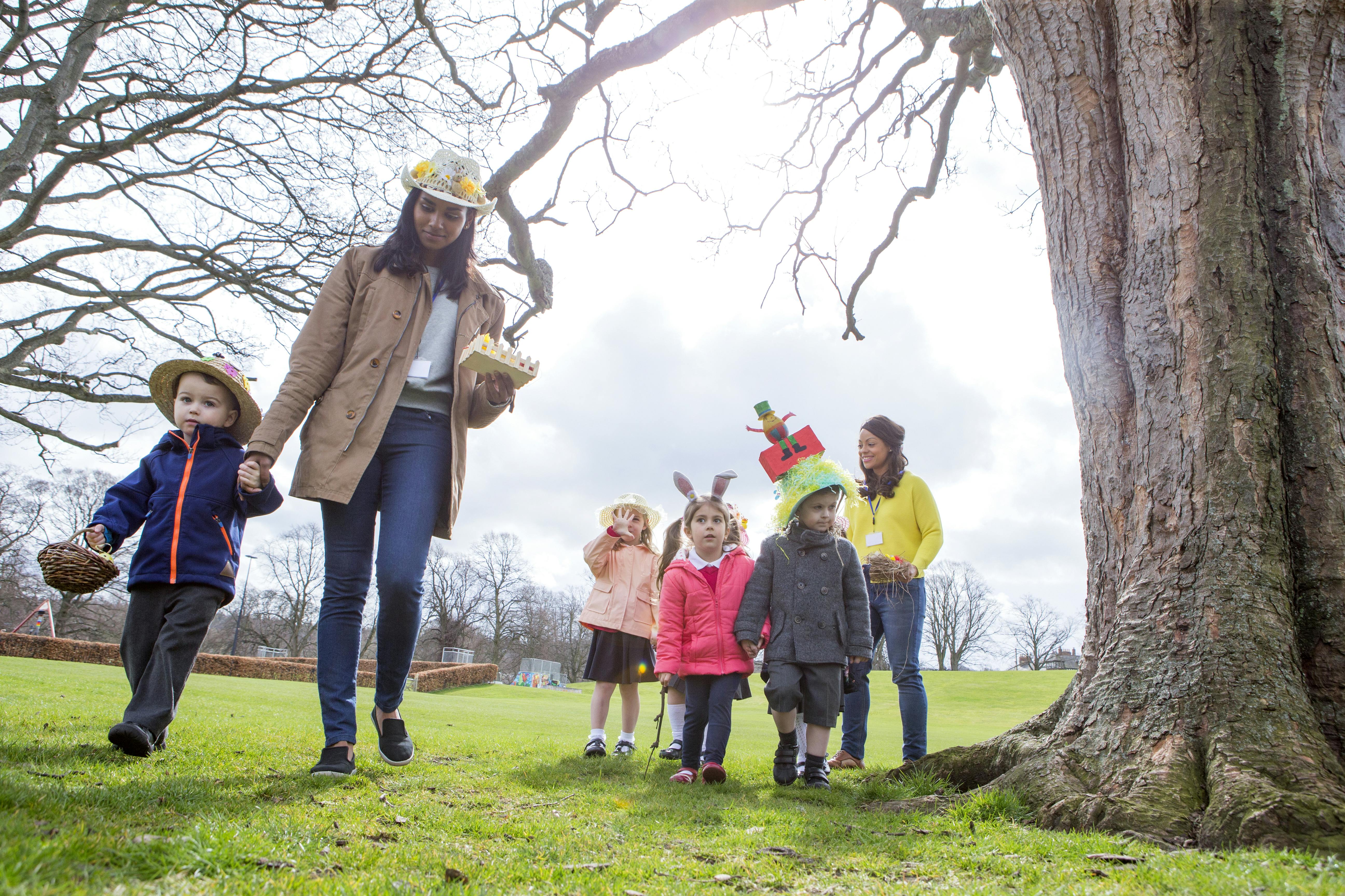 Deux assistantes maternelles promènent un petit groupe d'enfants à la recherche d'œufs de Pâques dans un parc.