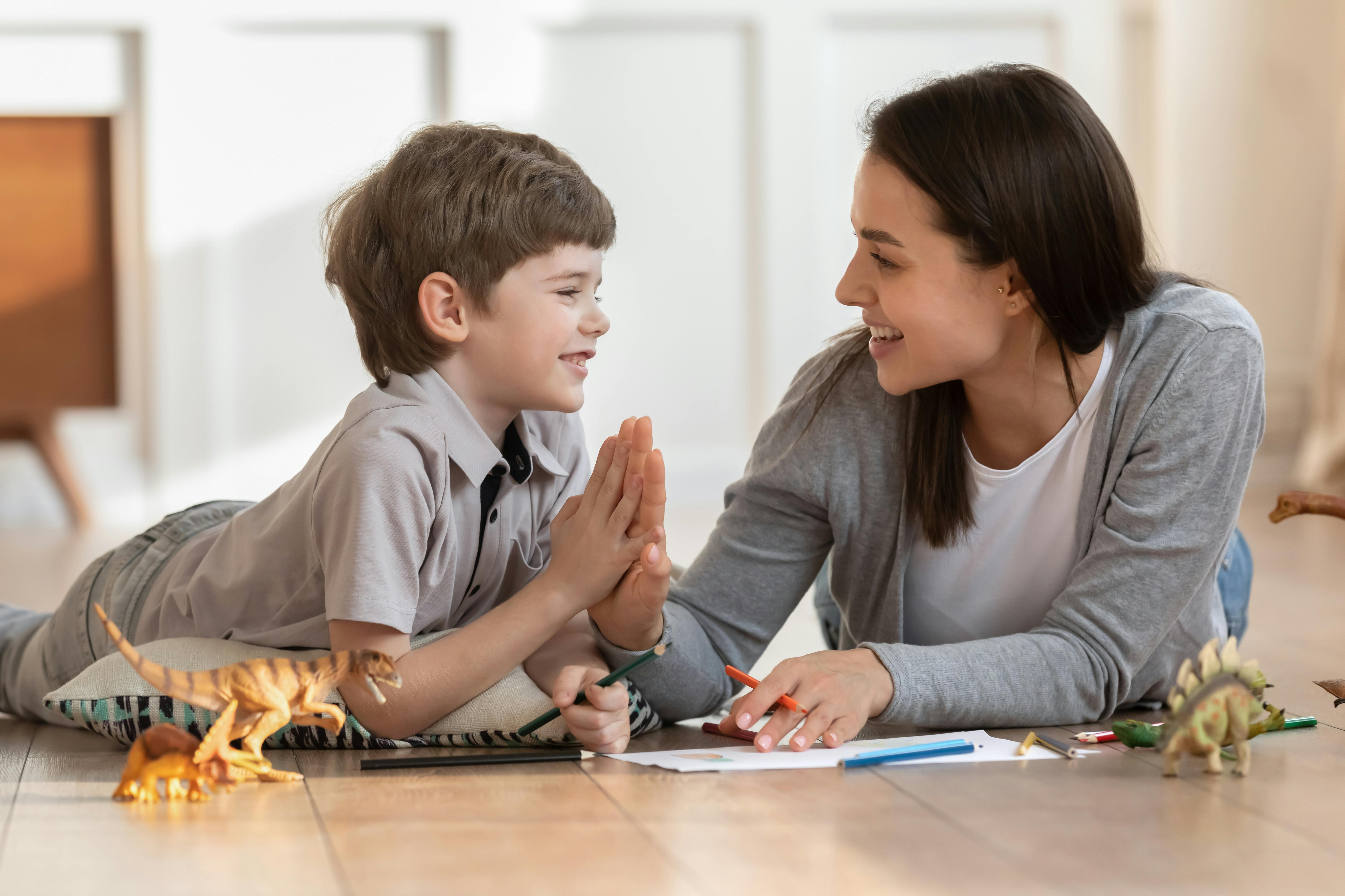 Un garçon et une femme partagent un moment de complicité en jouant avec des crayons et des figurines de dinosaures.