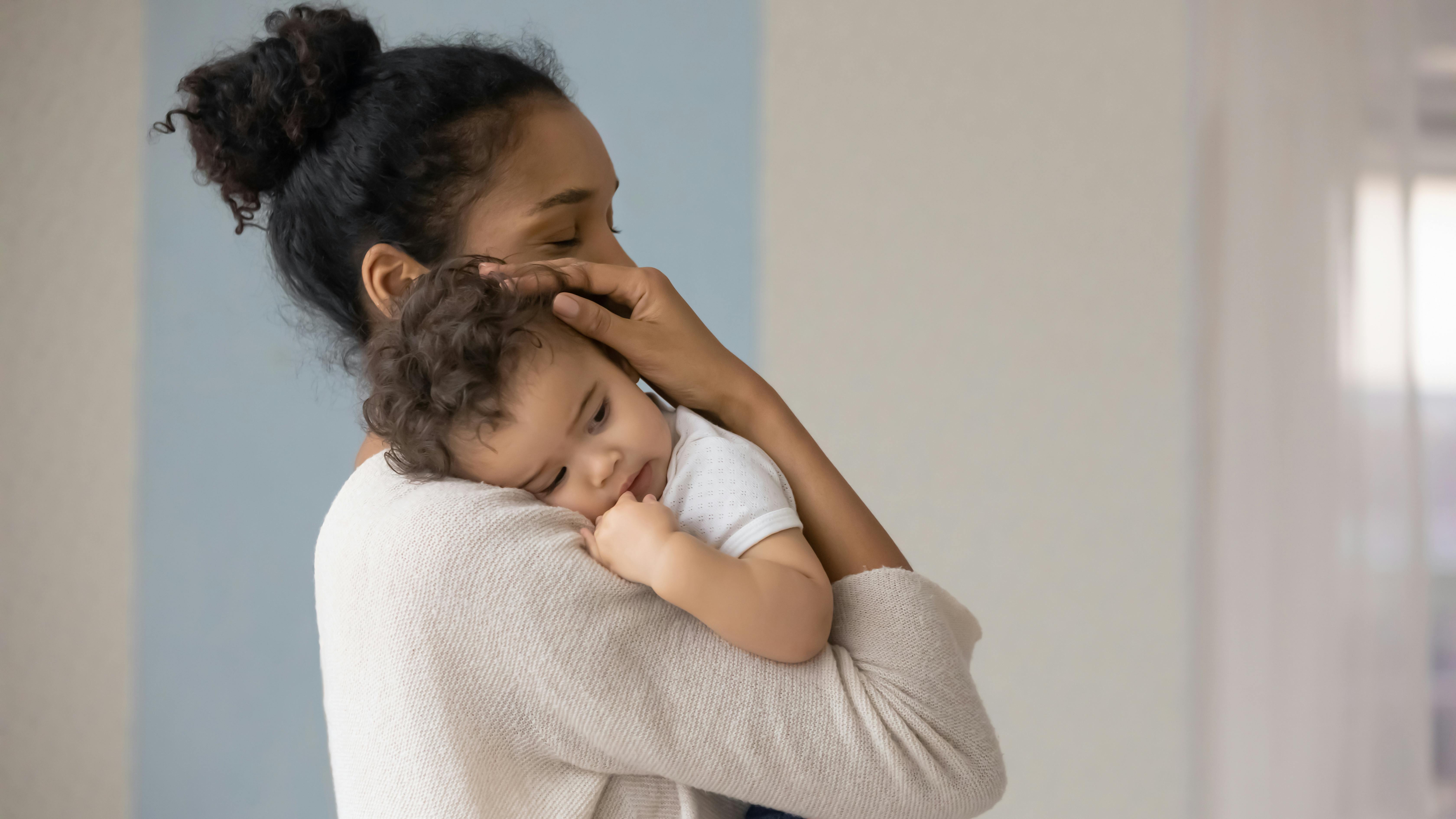 Une mère tient tendrement son bébé endormi contre elle.