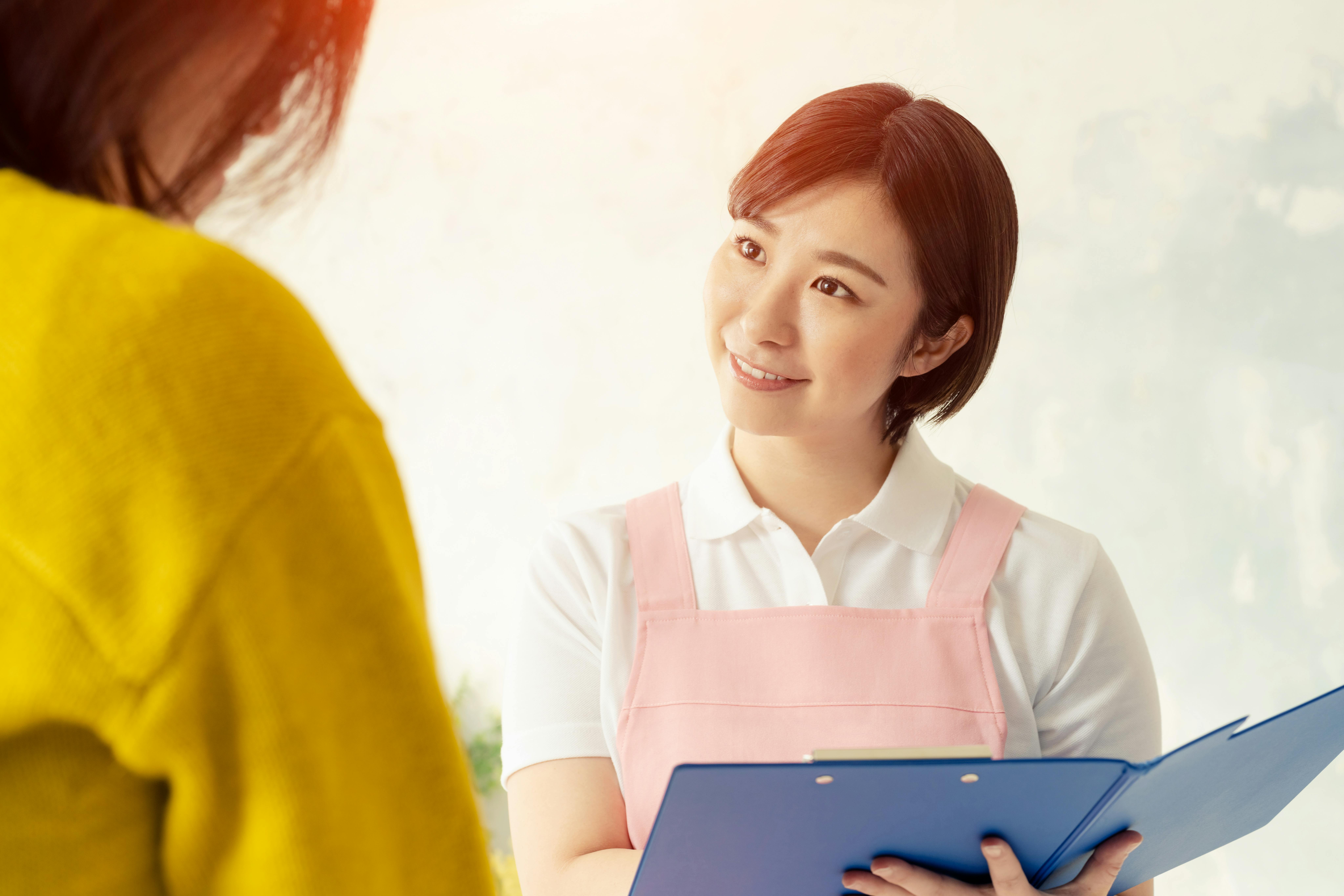 Une femme souriante tenant une tablette fait face à une autre femme dans un cadre lumineux et accueillant, suggérant une interaction amicale ou professionnelle.