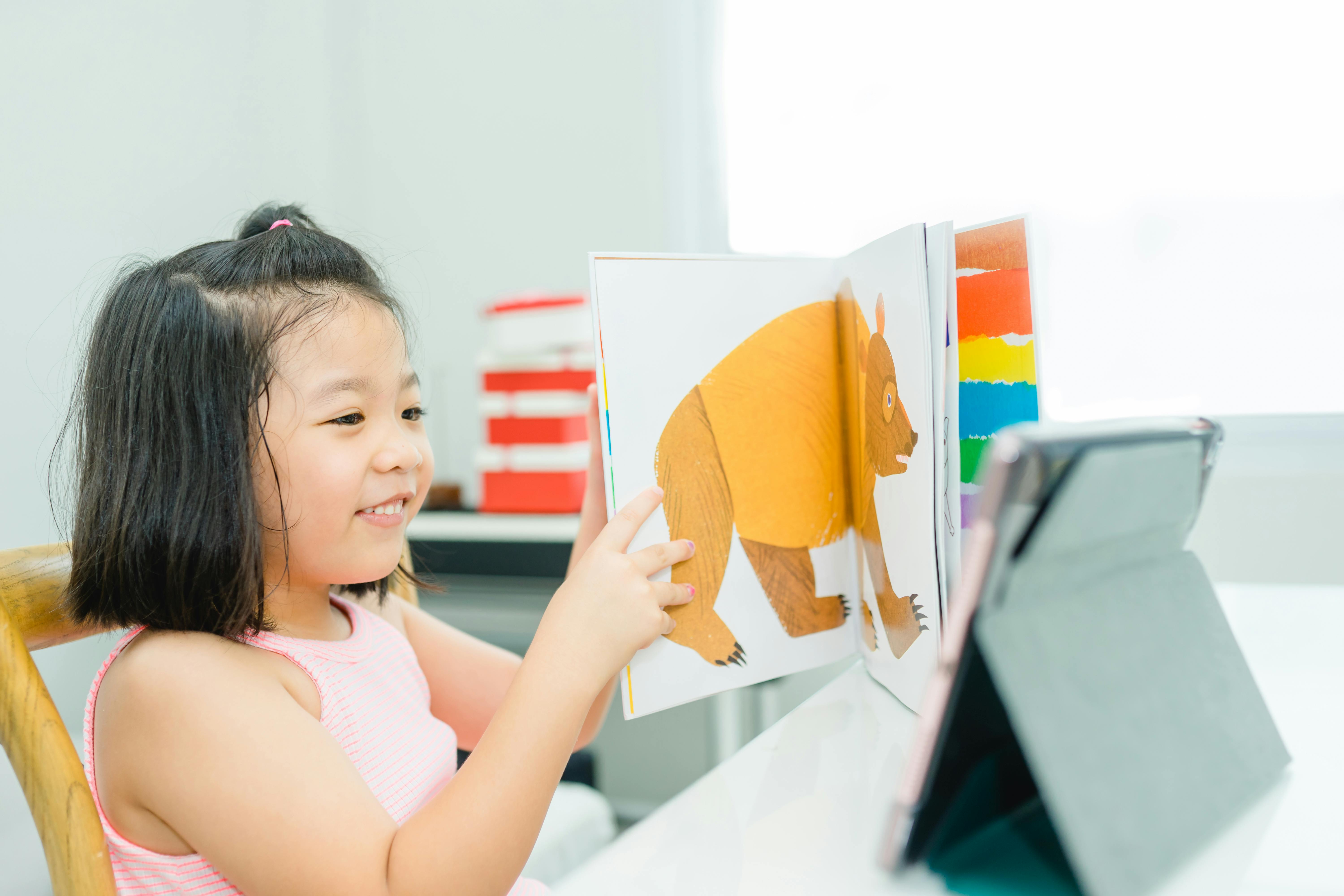 Une jeune fille souriante regarde un livre illustré en utilisant une tablette à la maison.