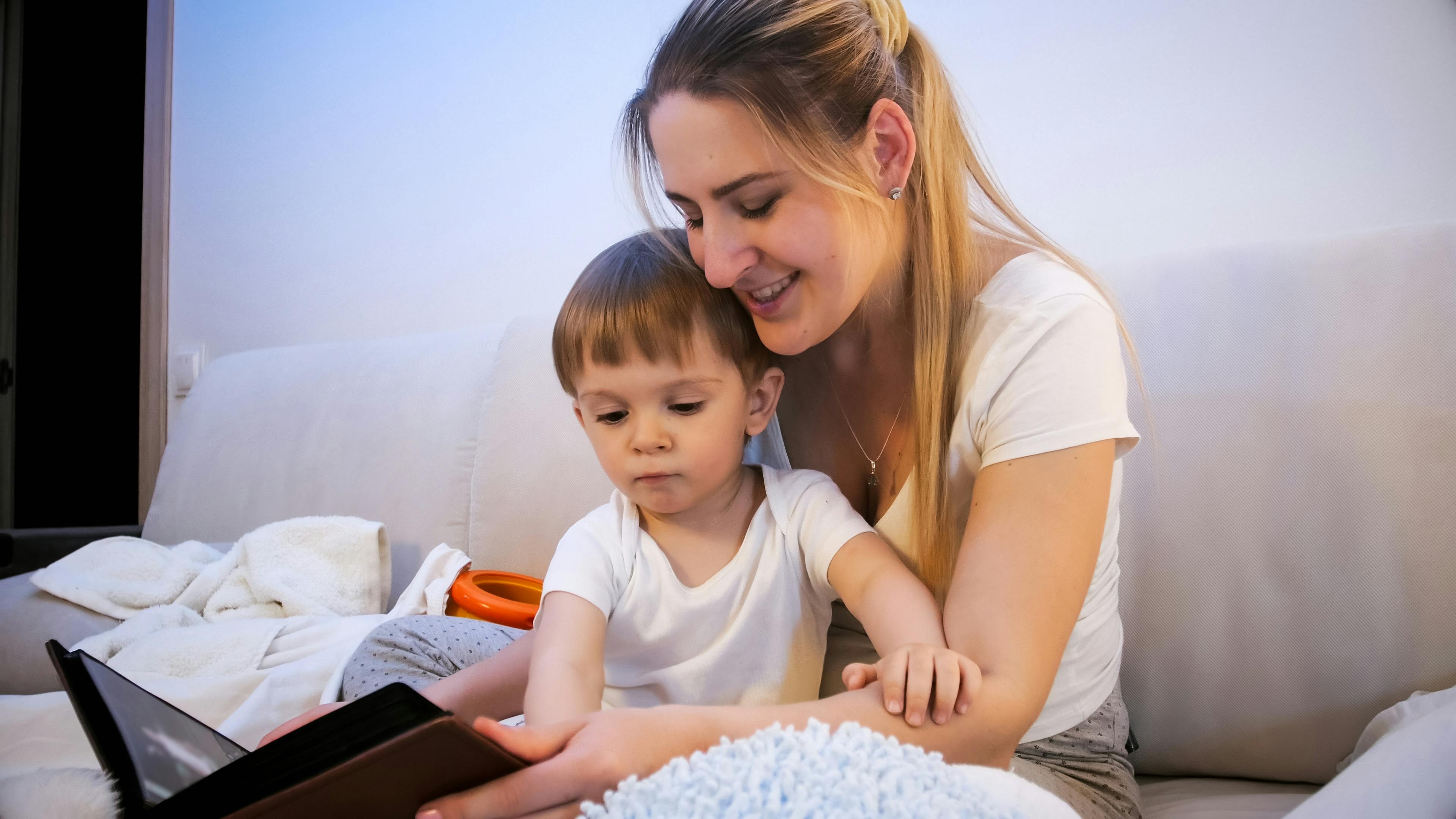 Une mère et son jeune enfant lisent ensemble sur un canapé.