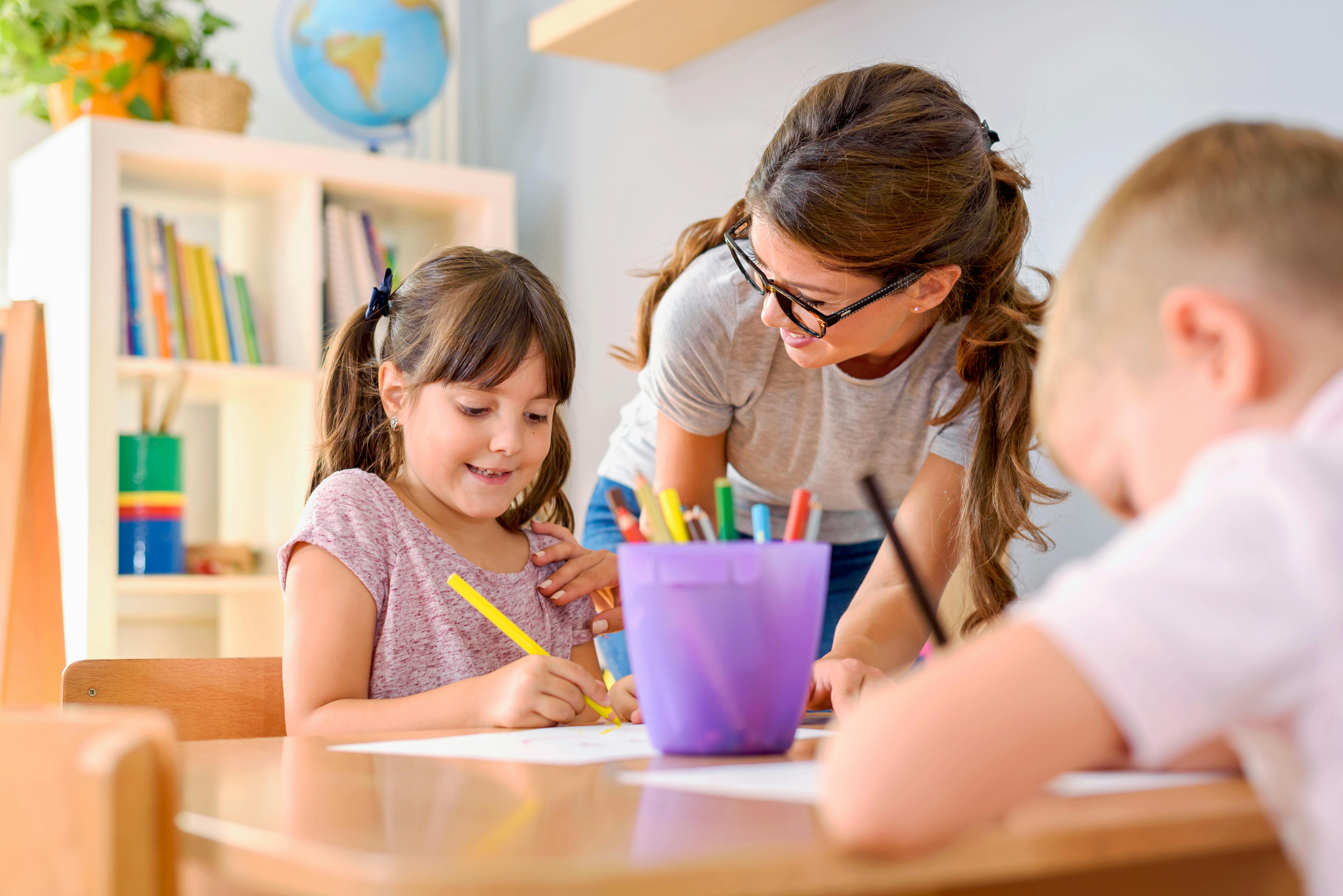 Une assistante maternelle supervise une jeune fille et un jeune garçon en train de faire du coloriage.