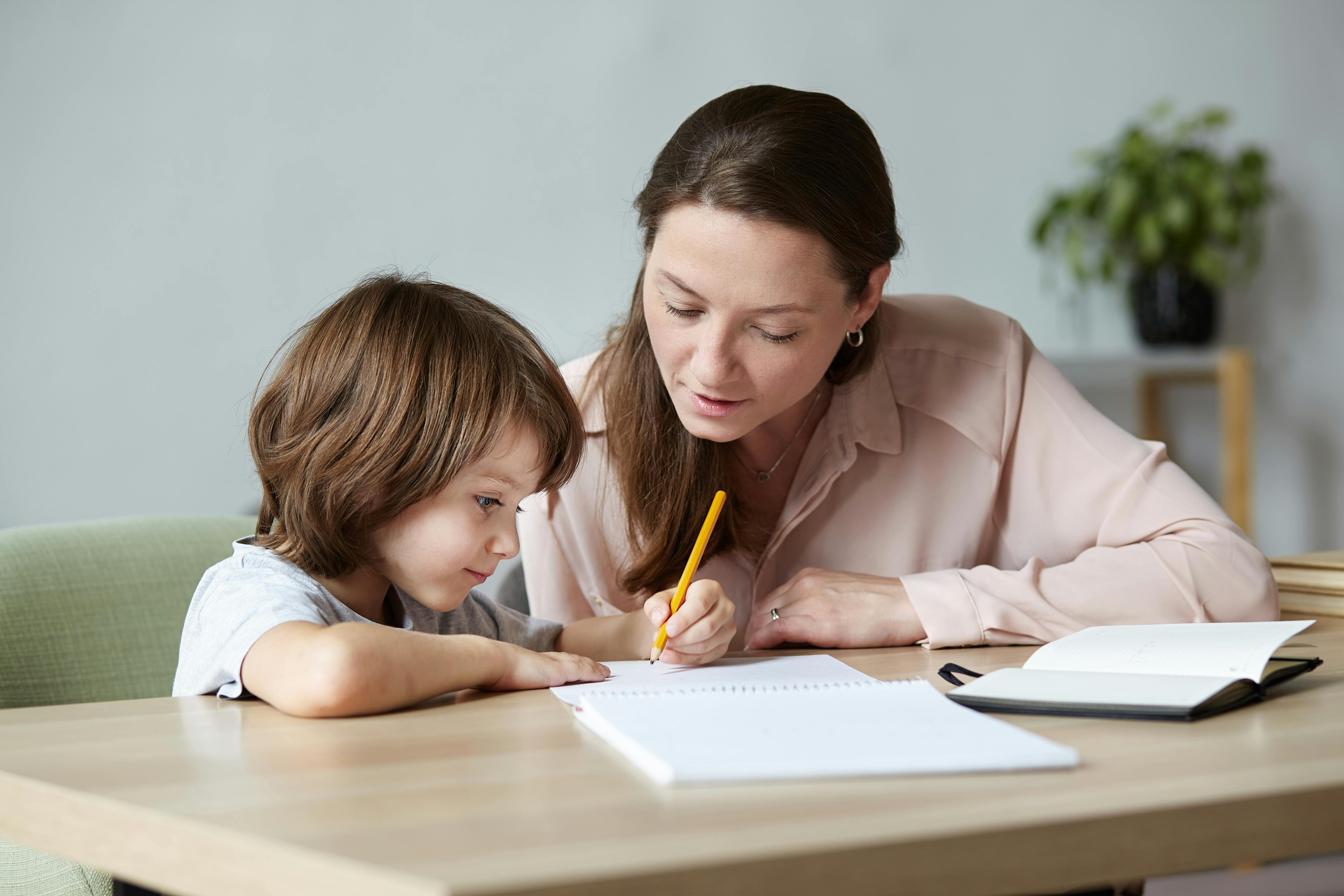 Une femme aide un enfant à faire ses devoirs à une table.