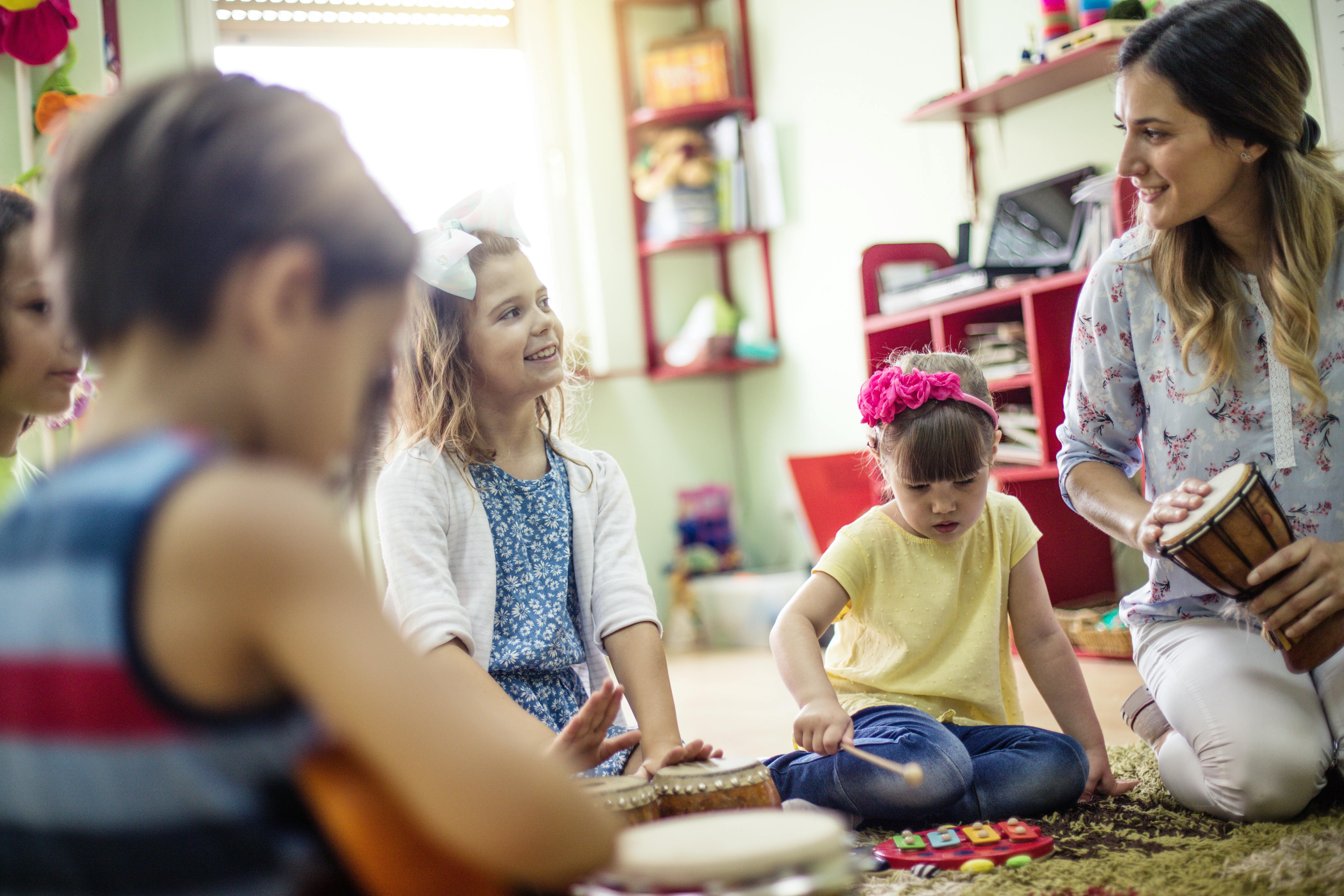 Une éducatrice joue des instruments de musique avec un groupe d'enfants, les encourageant à participer.