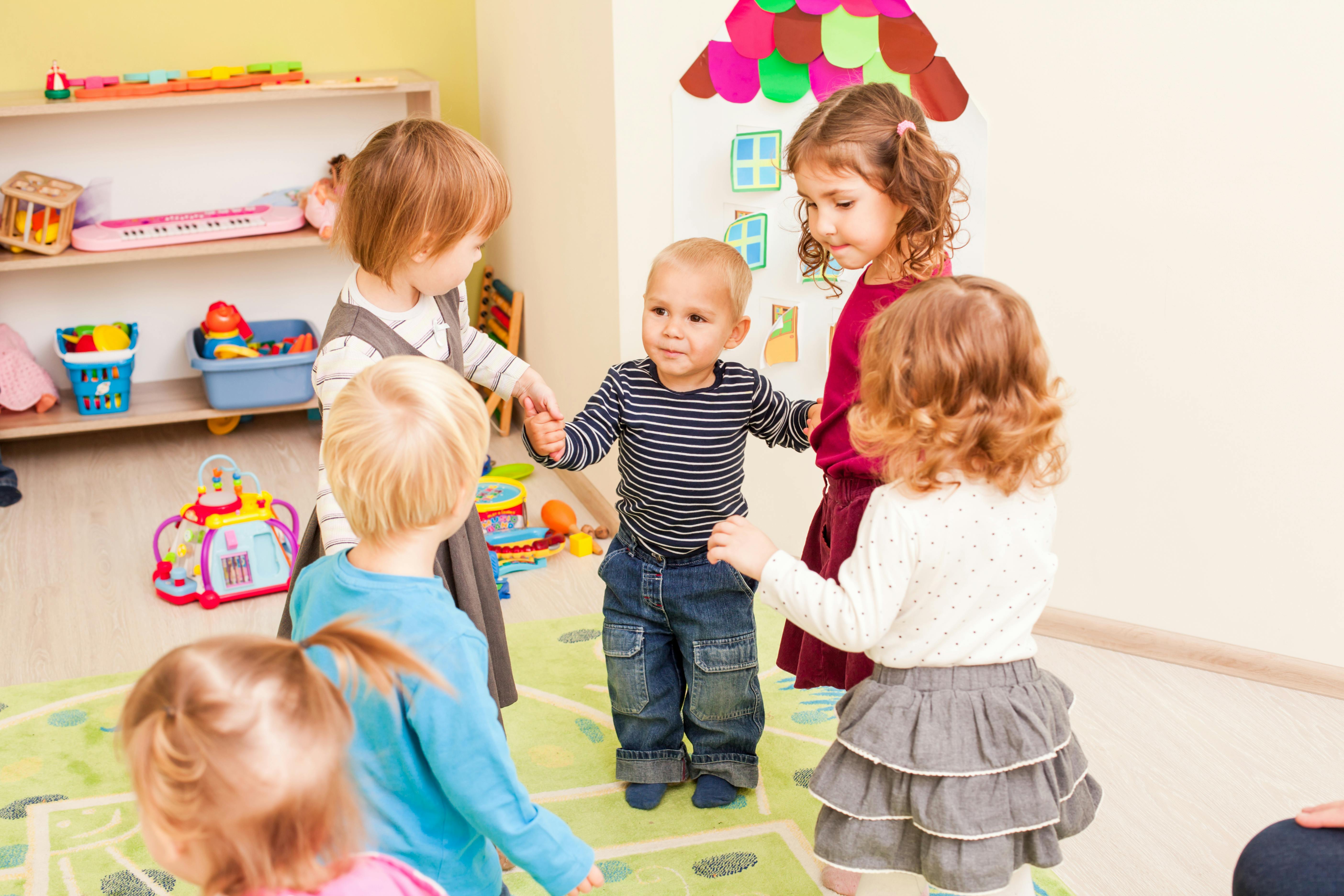 Un groupe de jeunes enfants jouant à faire la ronde dans une salle de classe lumineuse.