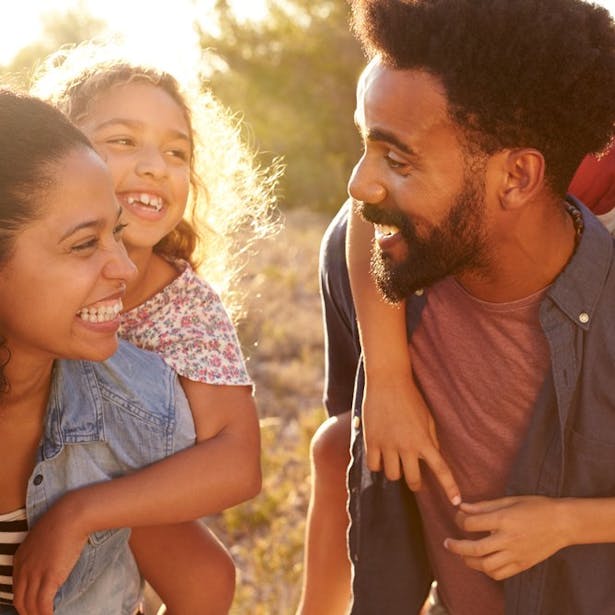Une famille heureuse lors d'une promenade , avec un père portant son fils sur son dos et une mère souriante tenant leur fille par la main.