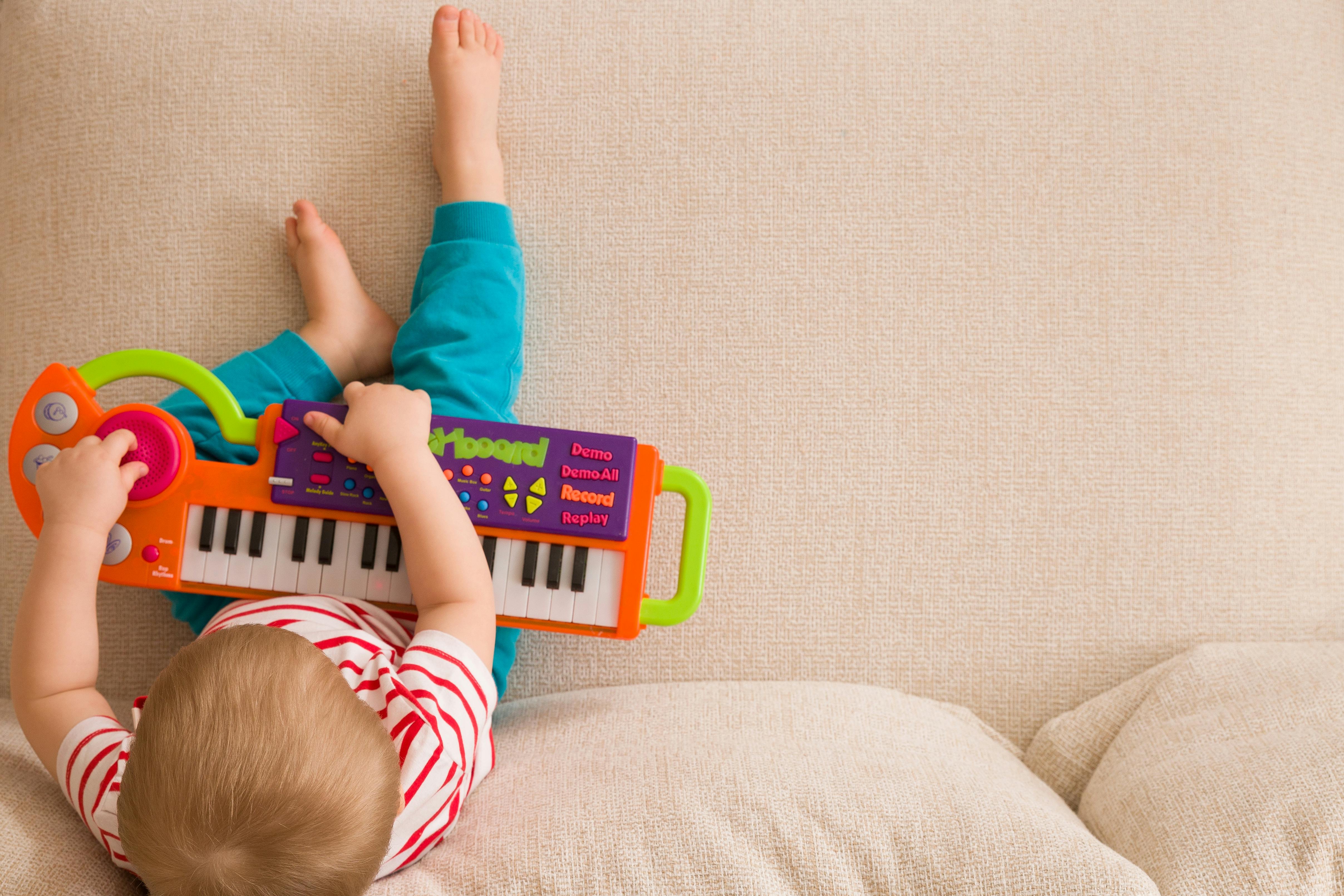 Un bébé joue avec un petit clavier jouet coloré, allongé sur un canapé.
