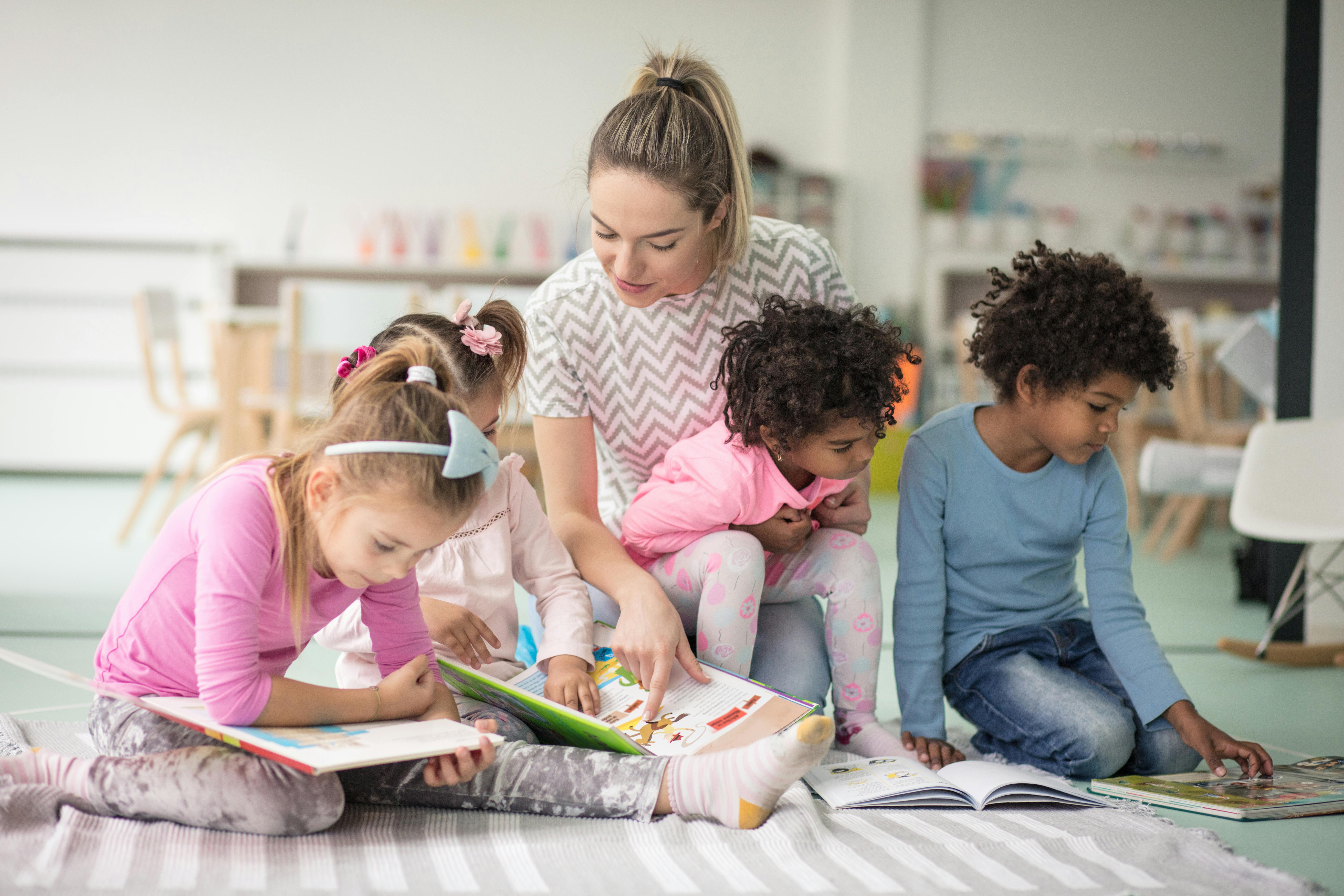 Une éducatrice lit un livre à trois enfants assis autour d'elle, dans une salle de classe lumineuse.