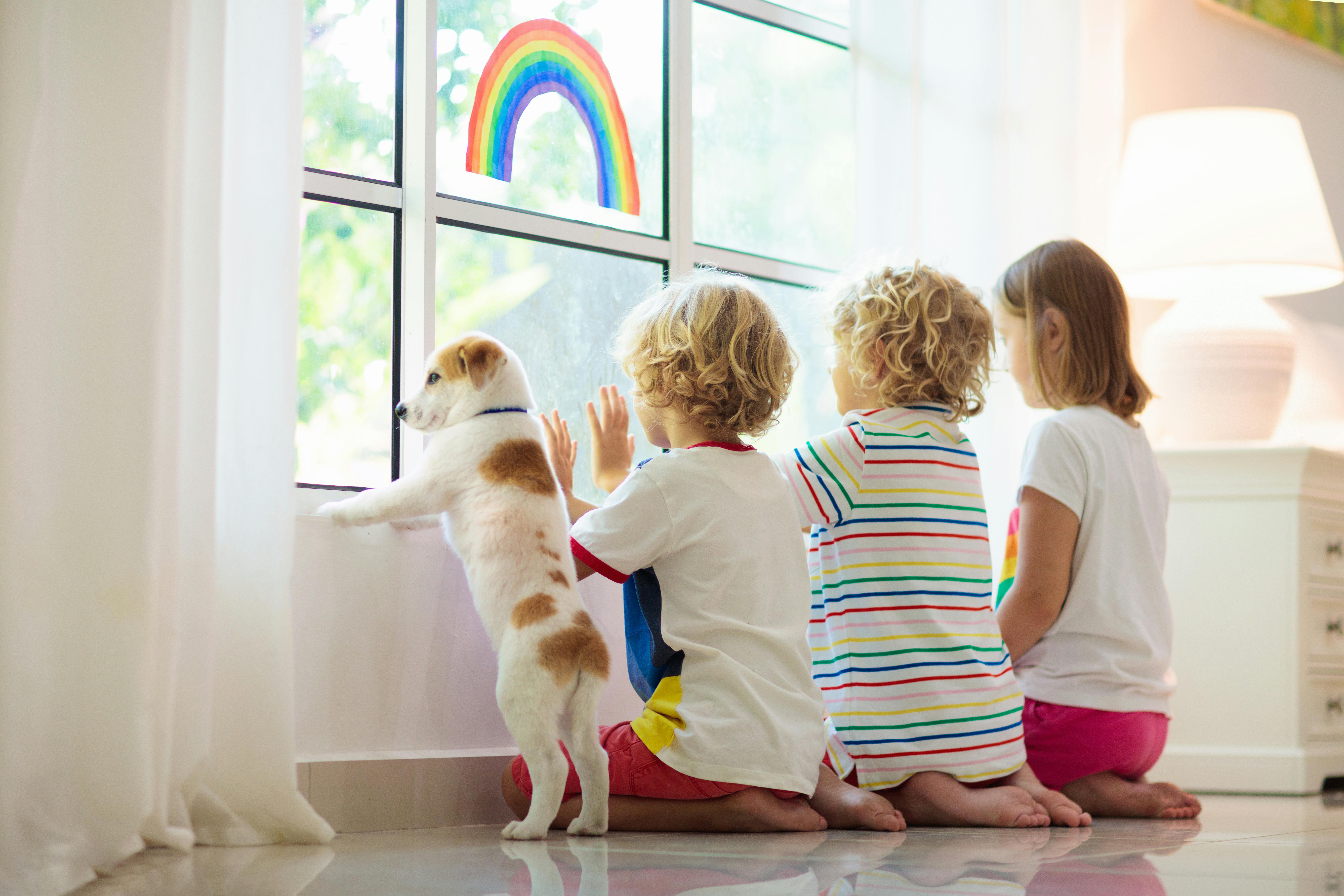 Trois enfants et un chien regardent par la fenêtre, observant quelque chose à l'extérieur.