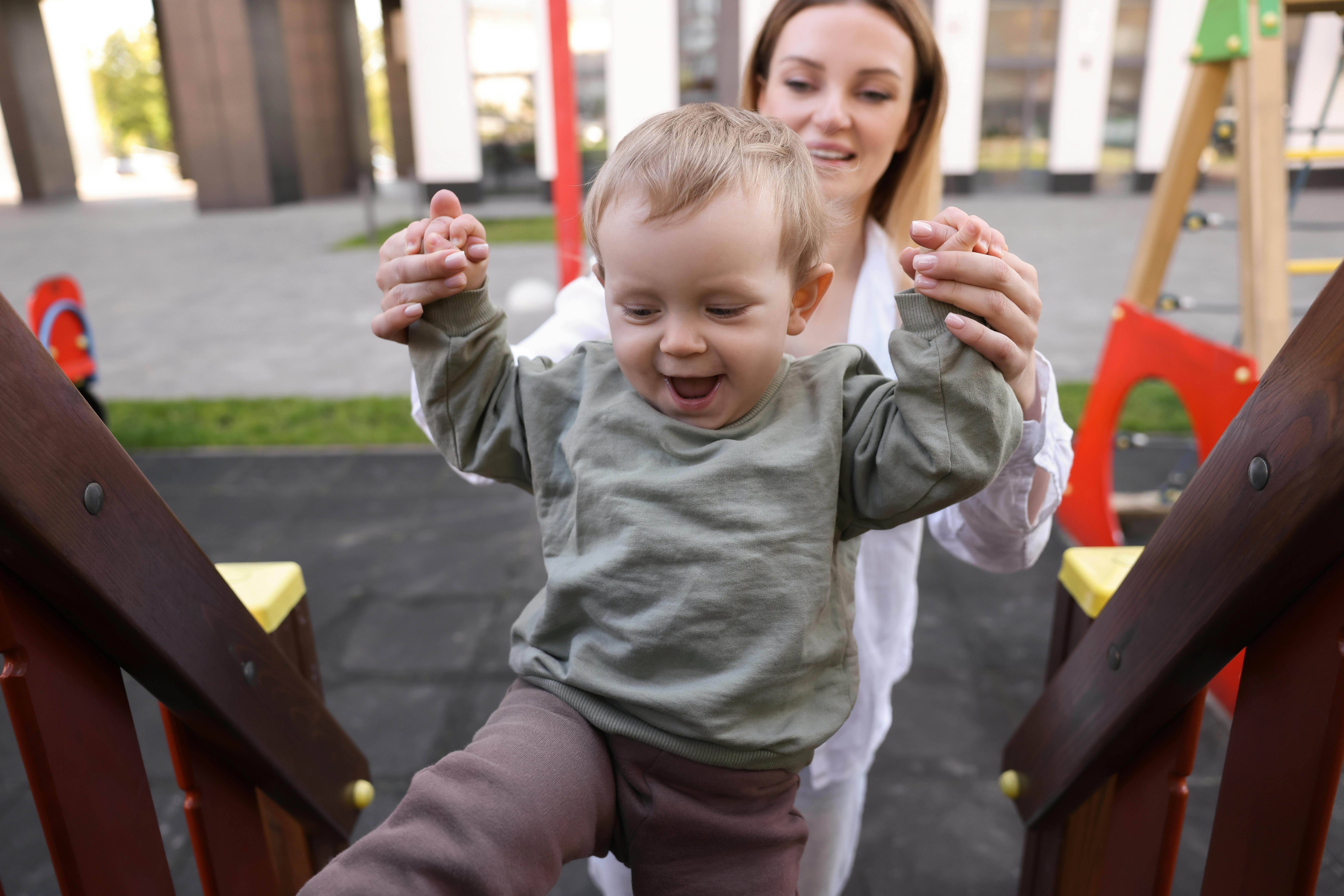 Une assistante maternelle joue avec l'enfant qu'elle garde dans un parc. L'enfant a l'air de beaucoup s'amuser.