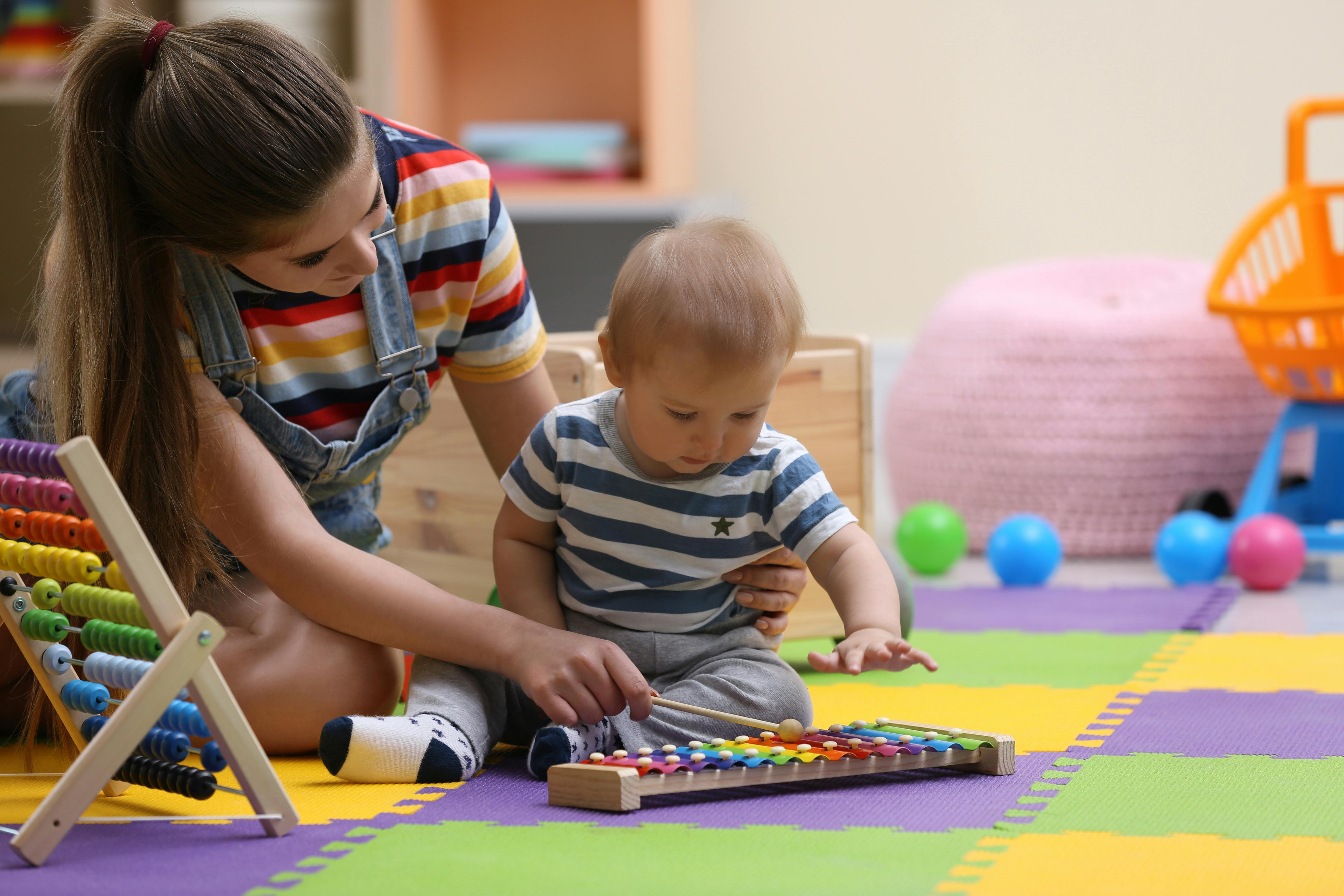 Une assistante maternelle apprend à un jeune garçon comment jouer du xylophone.