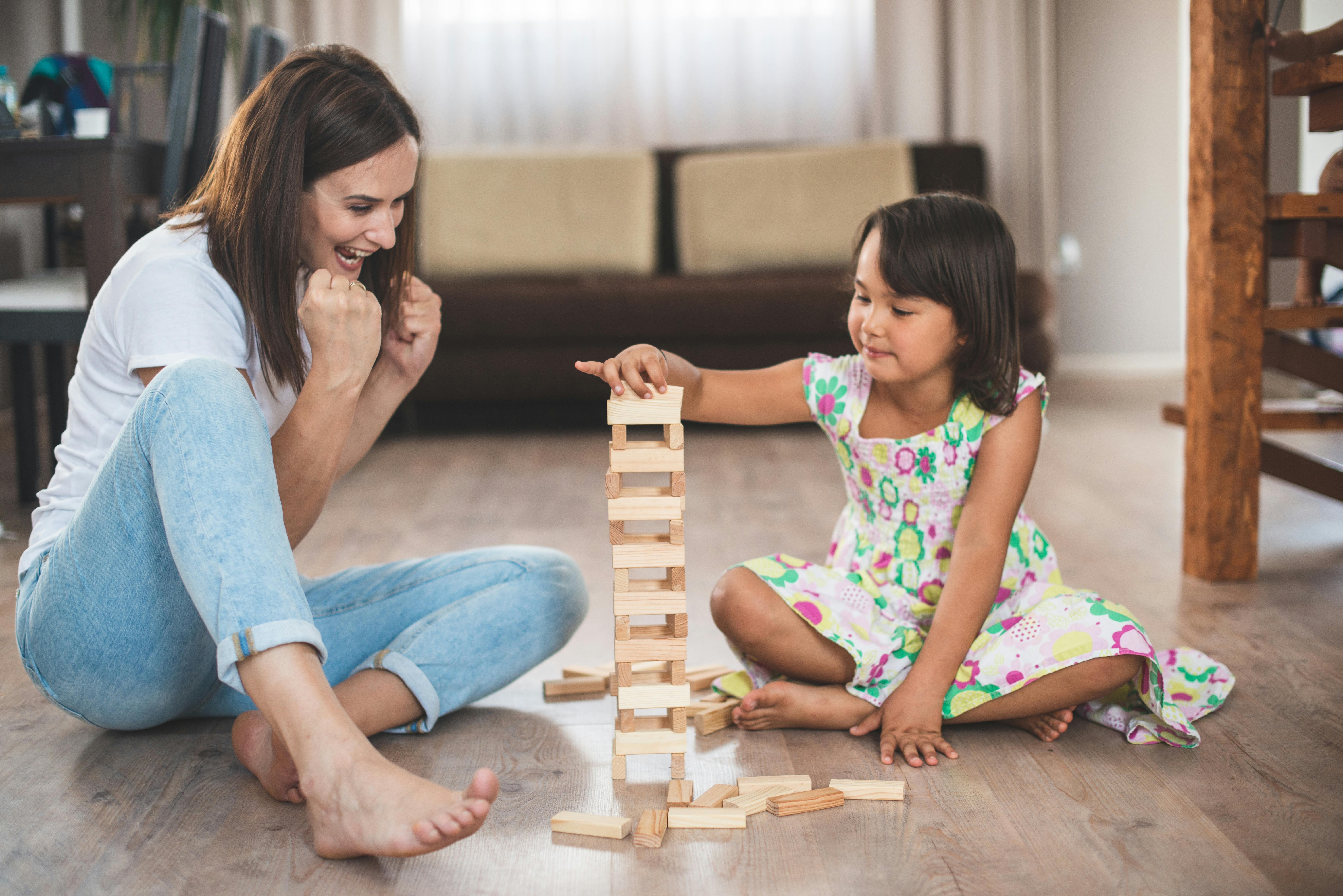 Une mère et sa fille jouent à un jeu de construction en bois sur le sol.