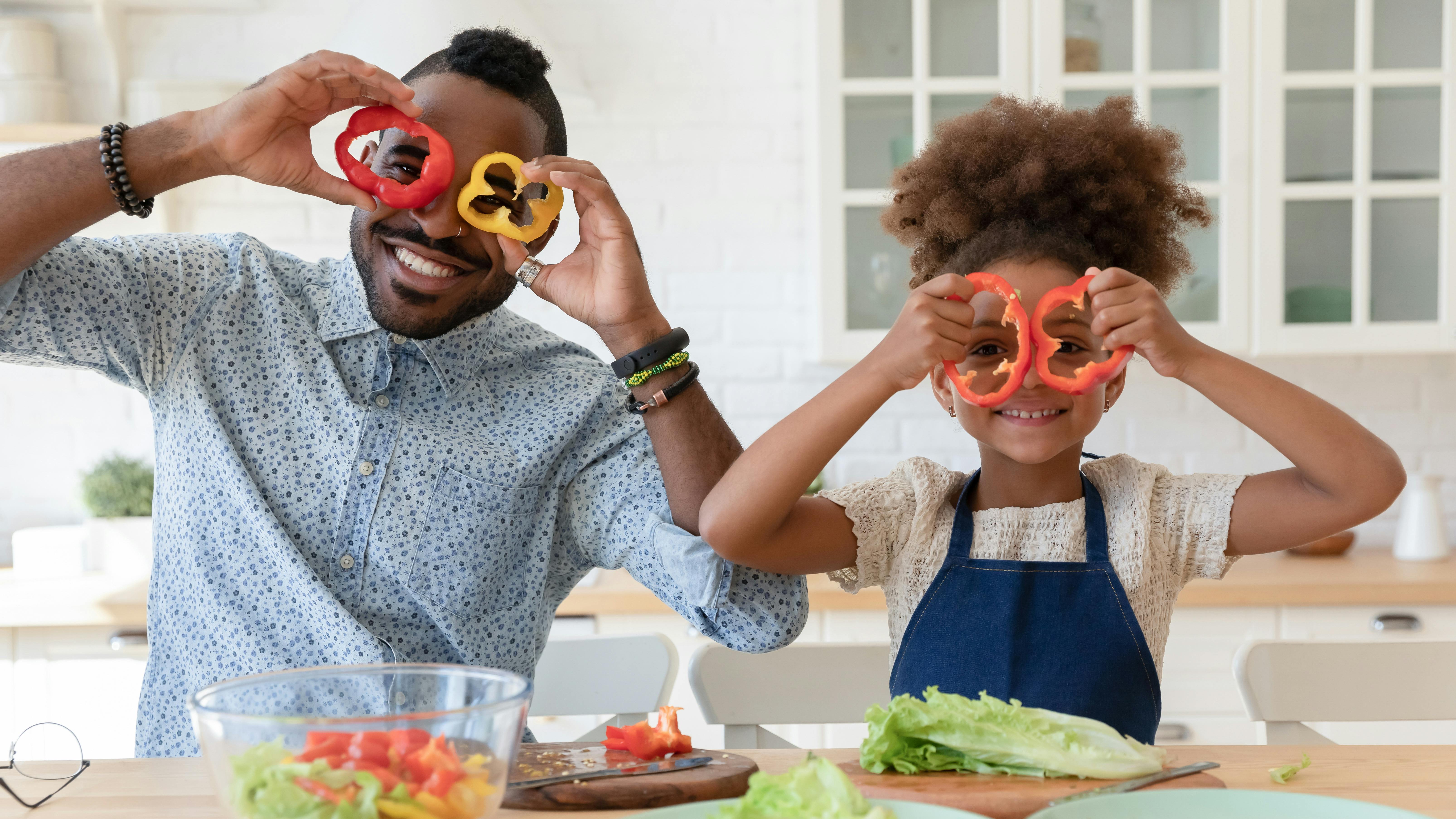 Un babysitter et la fille qu'il garde font la cuisine ensemble. Ils se font des lunettes avec des poivrons.