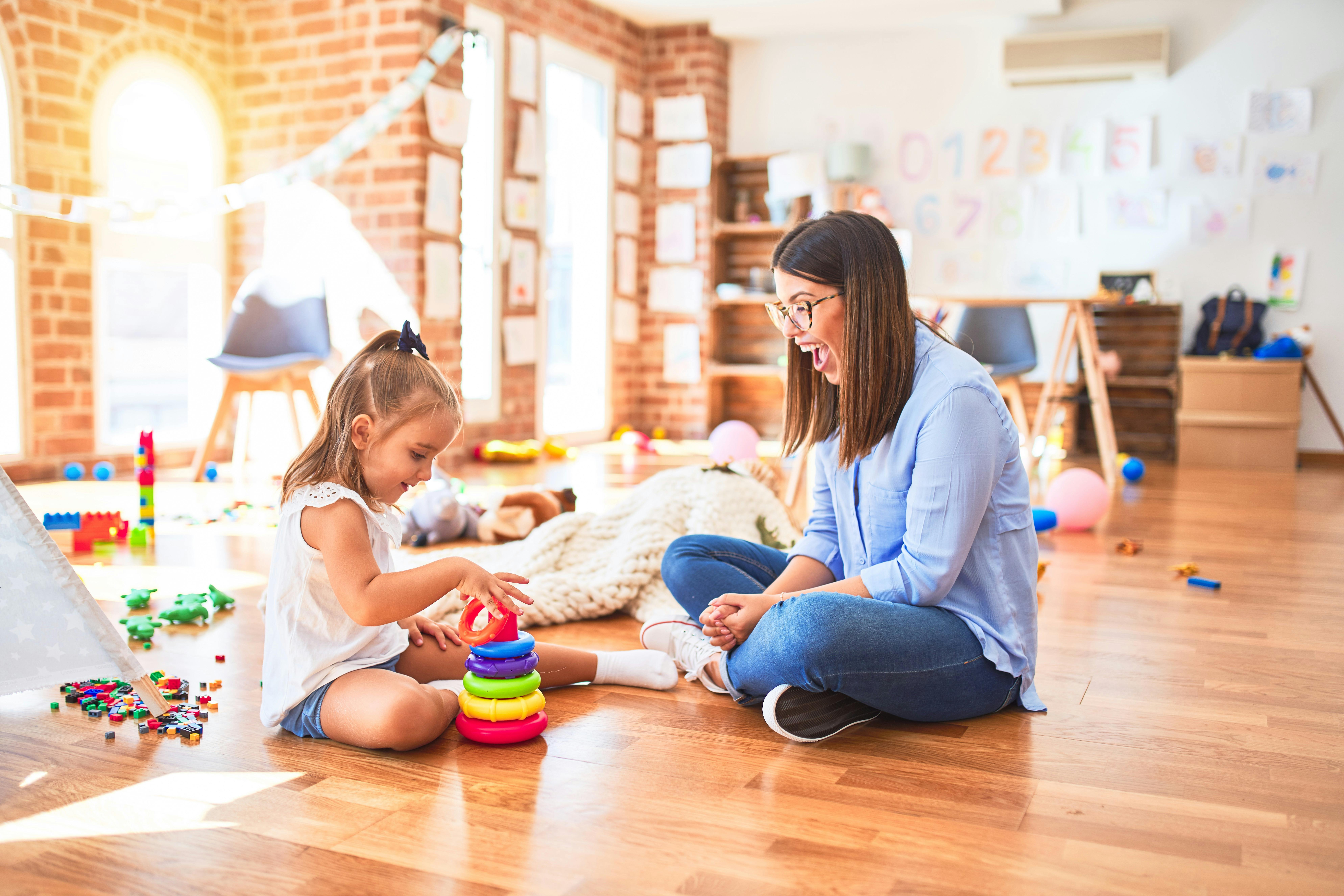 Dans une crèche, une petite fille et son assistante maternelle jouent ensemble.