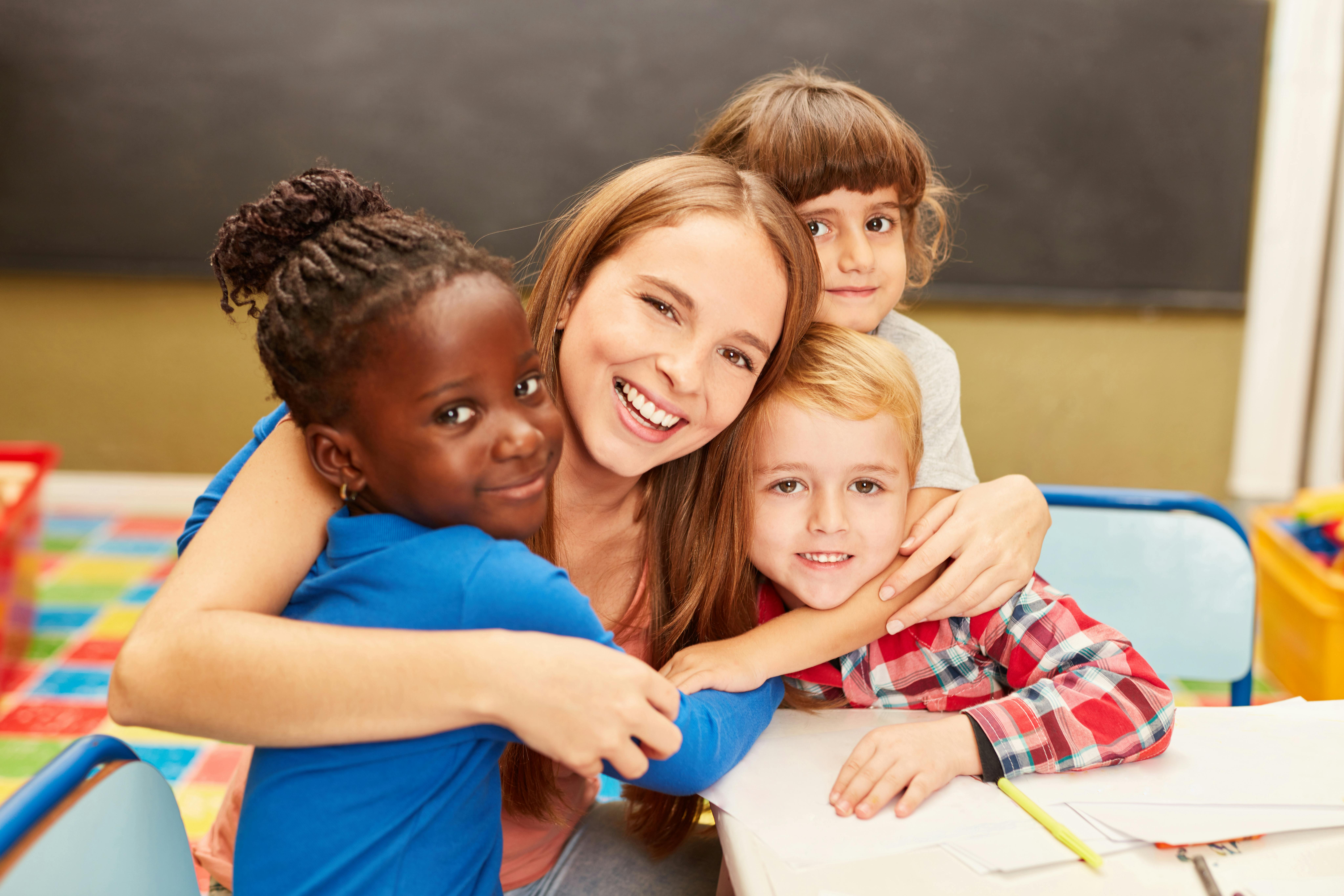 Une assistante maternelle embrasse trois enfants dans une salle de crèche. Tout le monde a l'air heureux.