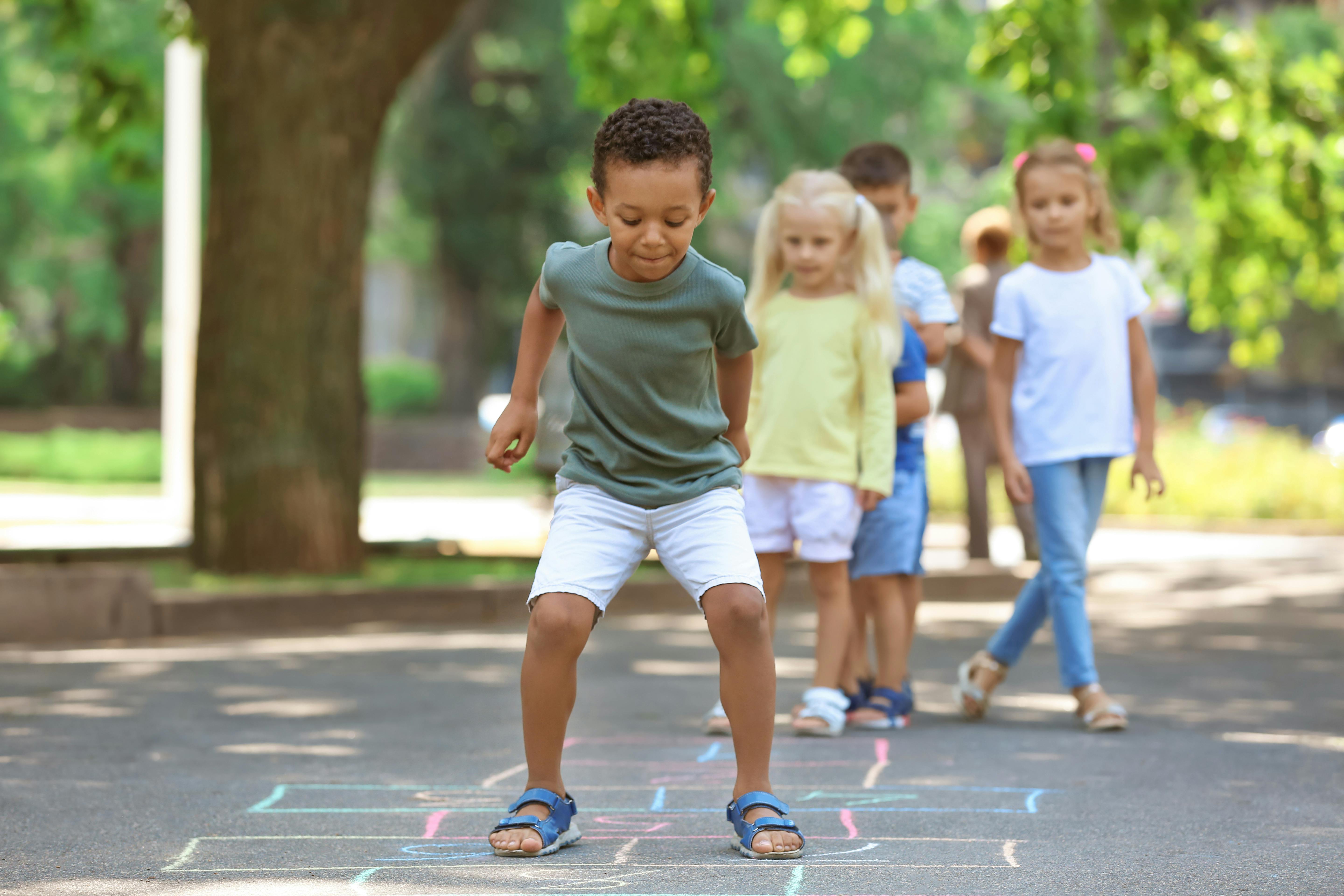 Un groupe d'enfants joue à la marelle dans une cour.