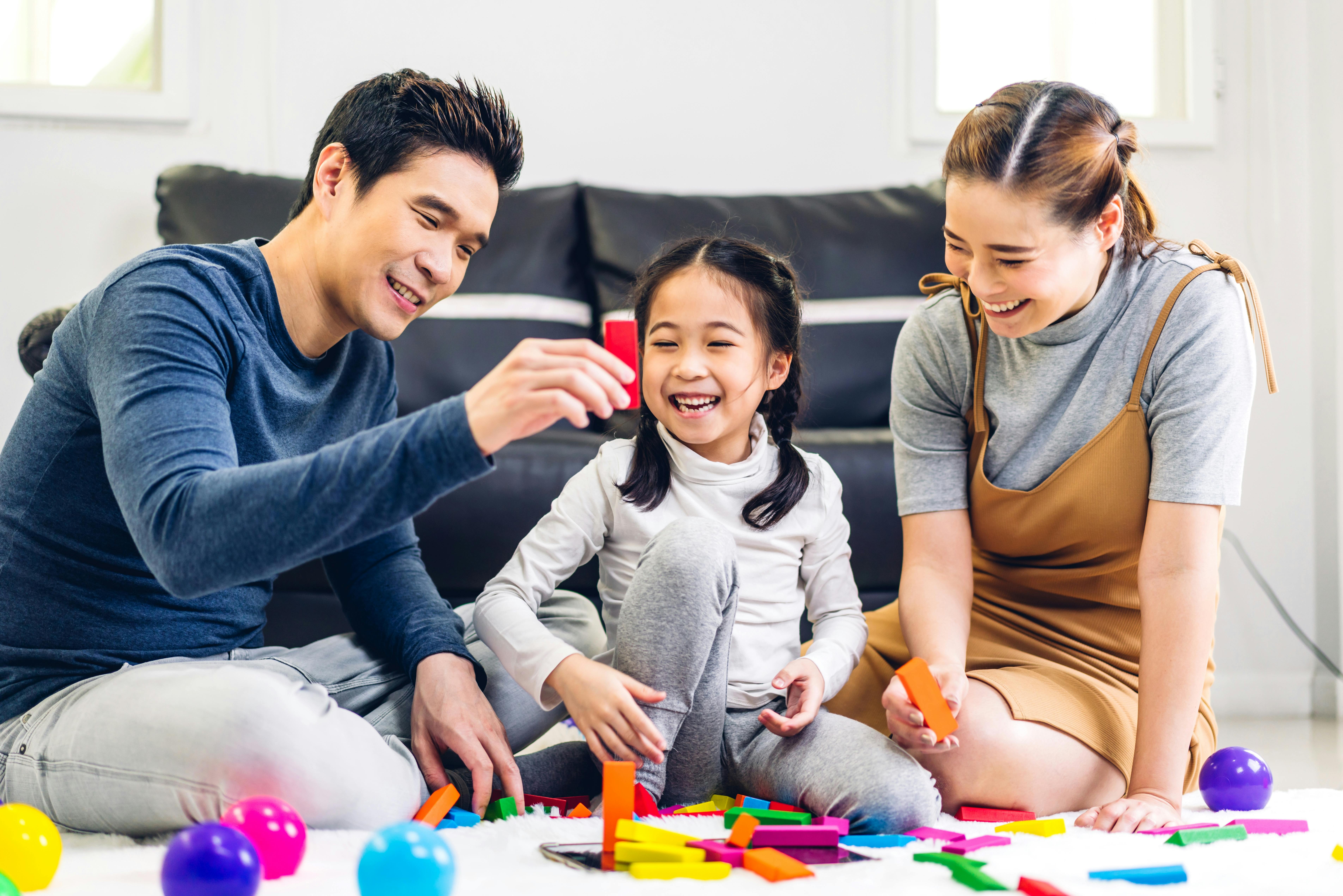 Une petite fille joue avec son père et sa mère avec des blocs en bois colorés. Ils sont assis par terre dans leur salon.