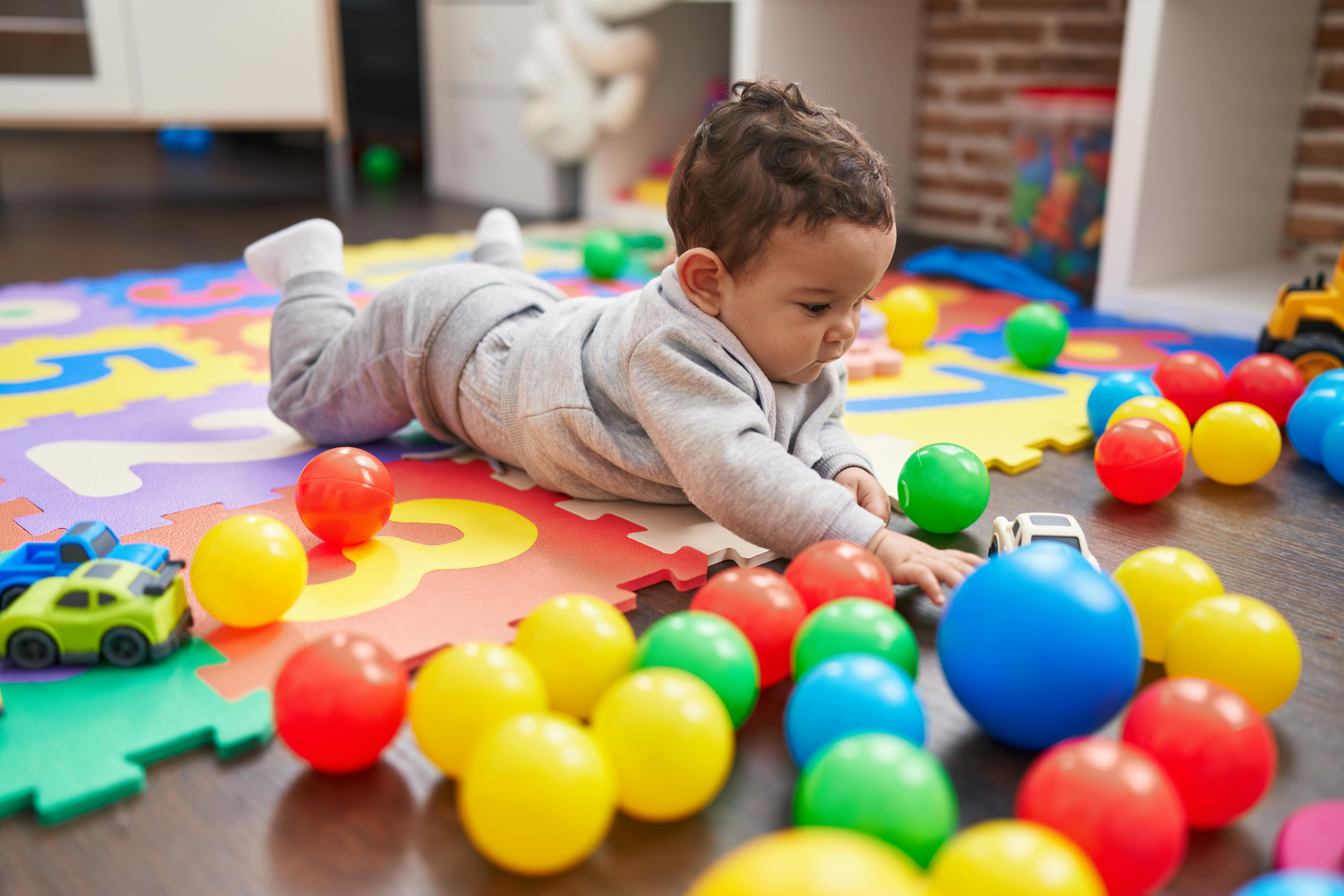 Un bébé joue avec des balles colorées et des jouets sur un tapis de jeu en mousse.