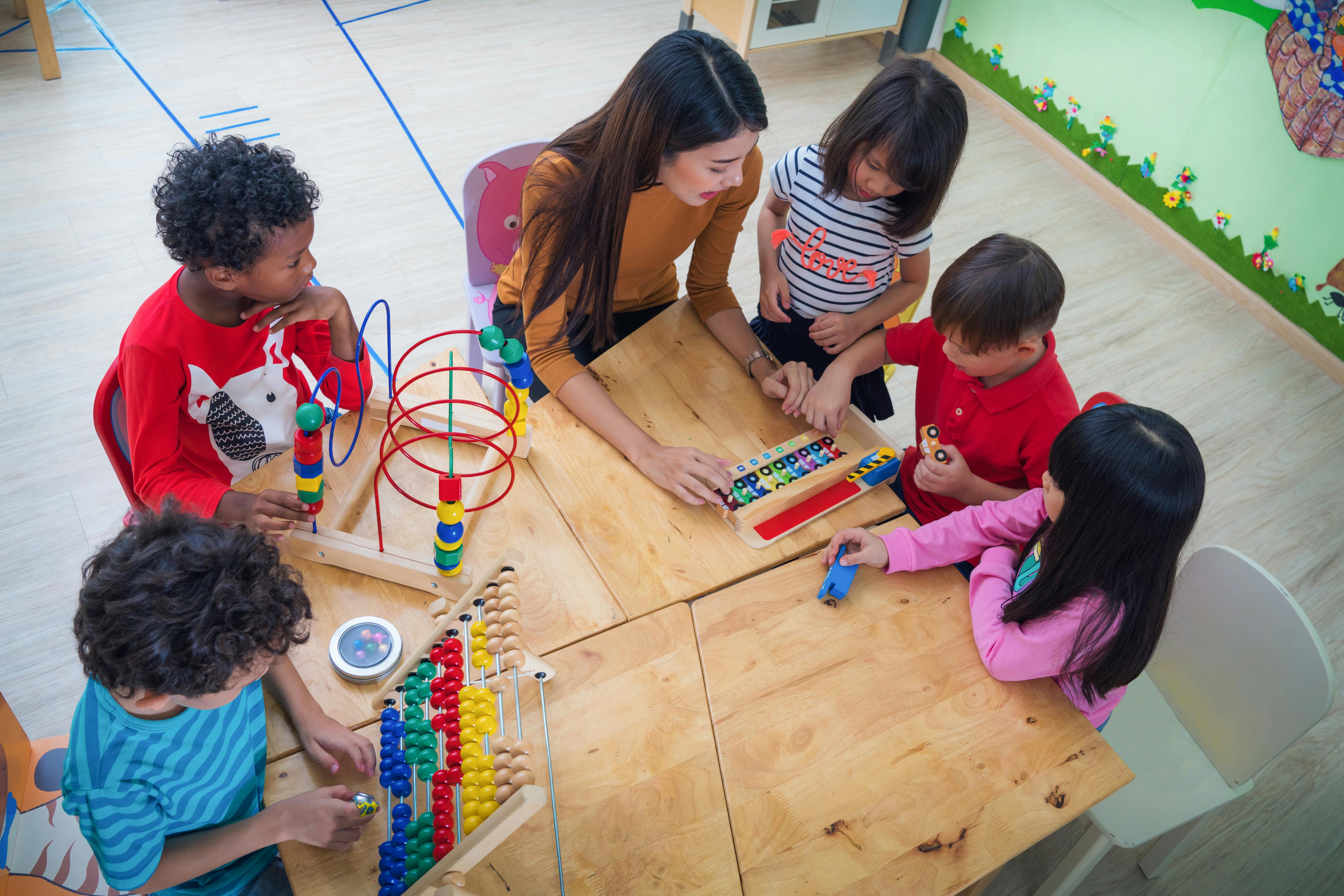 Une enseignante jouant à des jeux éducatifs avec des enfants autour d'une table dans une salle de classe.