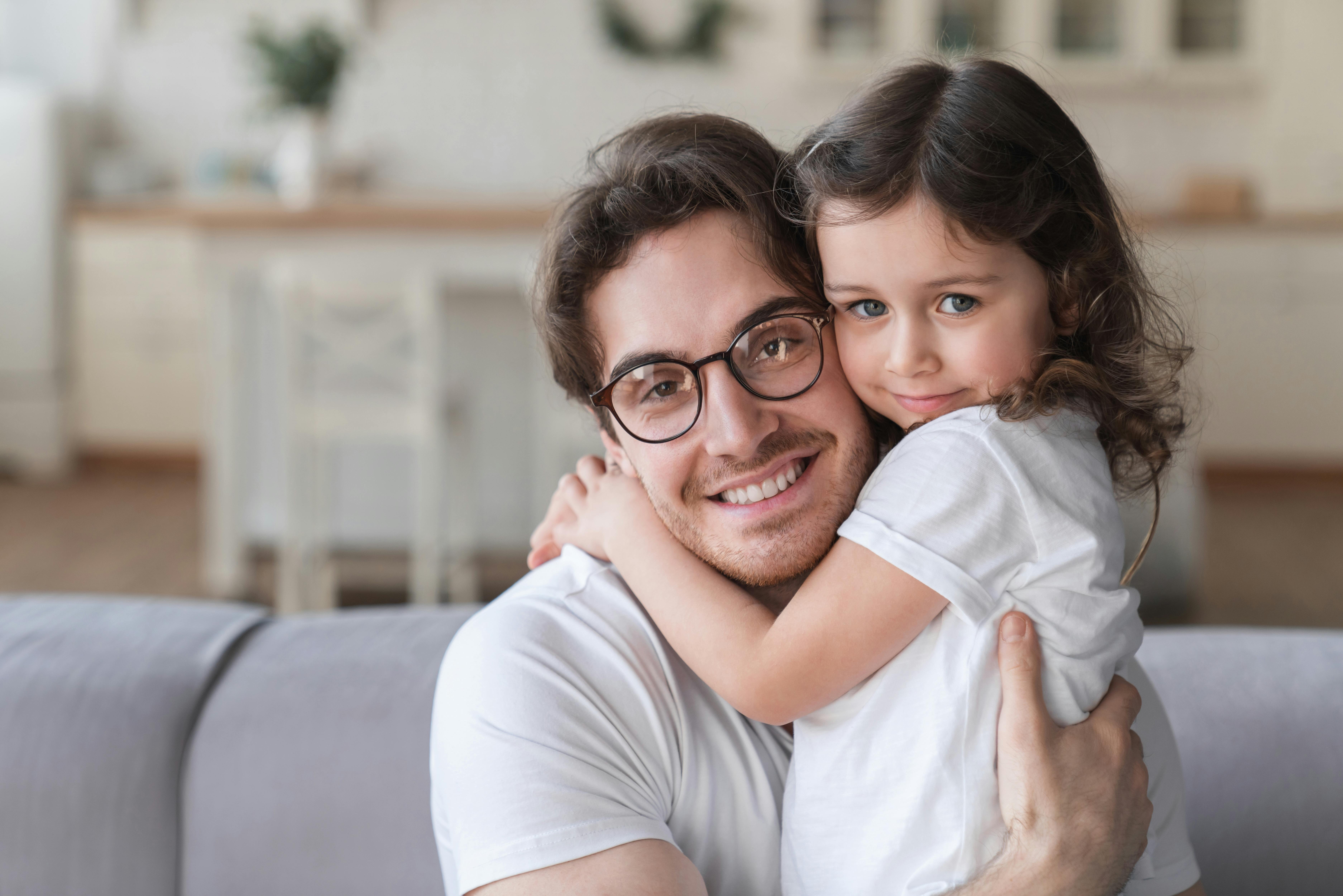 Un père souriant tient sa fille dans ses bras dans un salon.