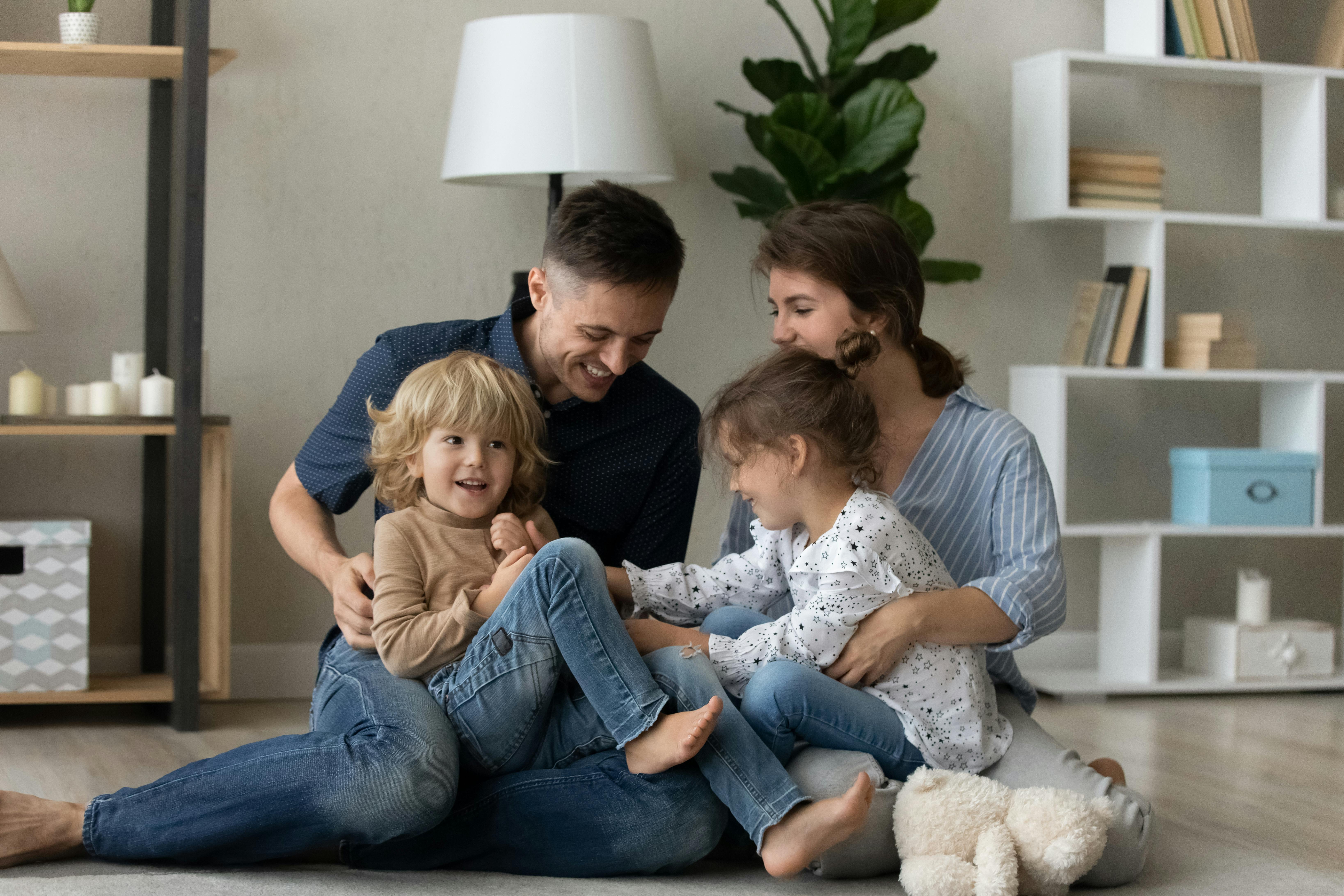 Une famille heureuse est assise sur le sol, riant ensemble dans un salon moderne.