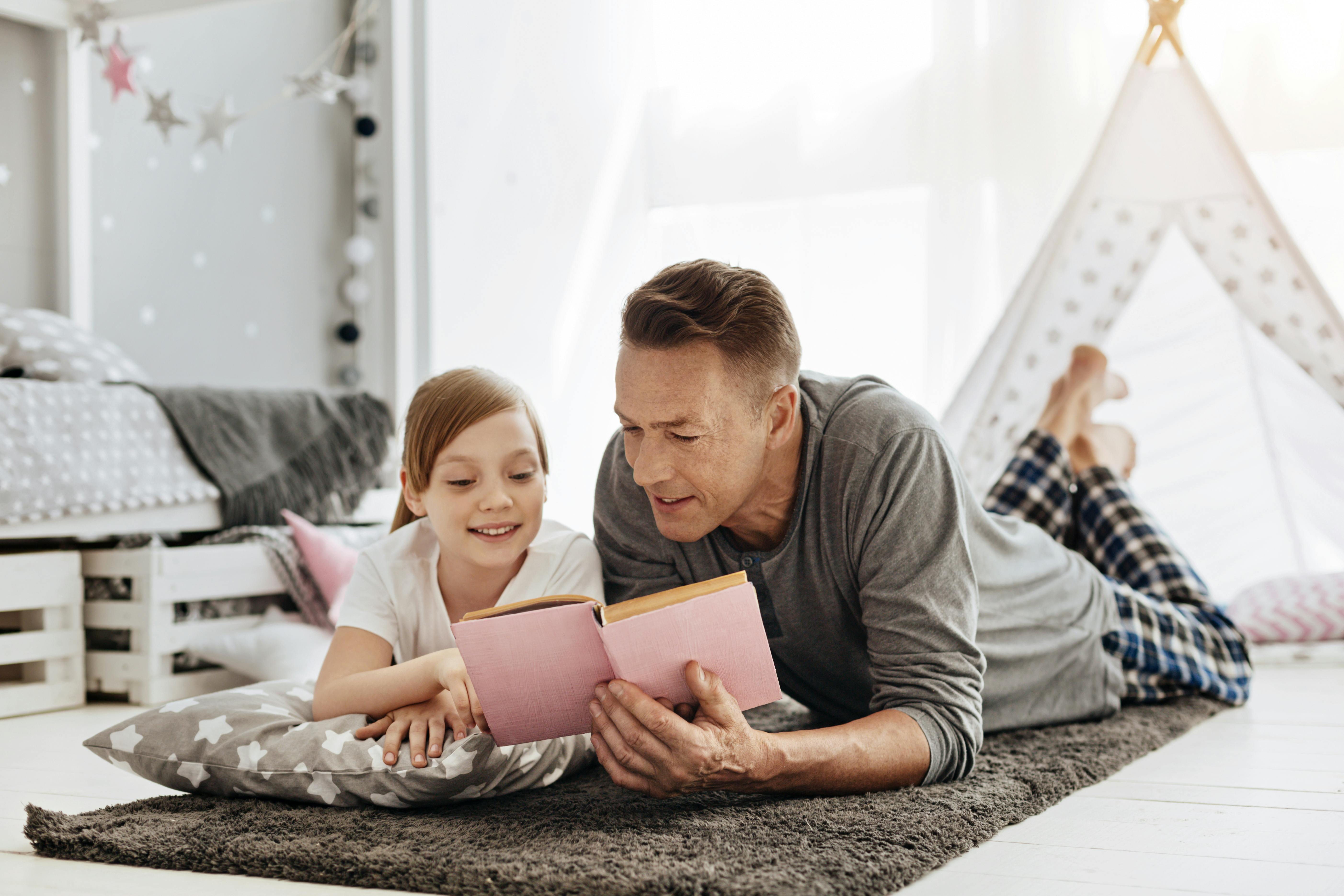Un baby-sitter et sa fille lisent ensemble sur le tapis d'une chambre d'enfant.