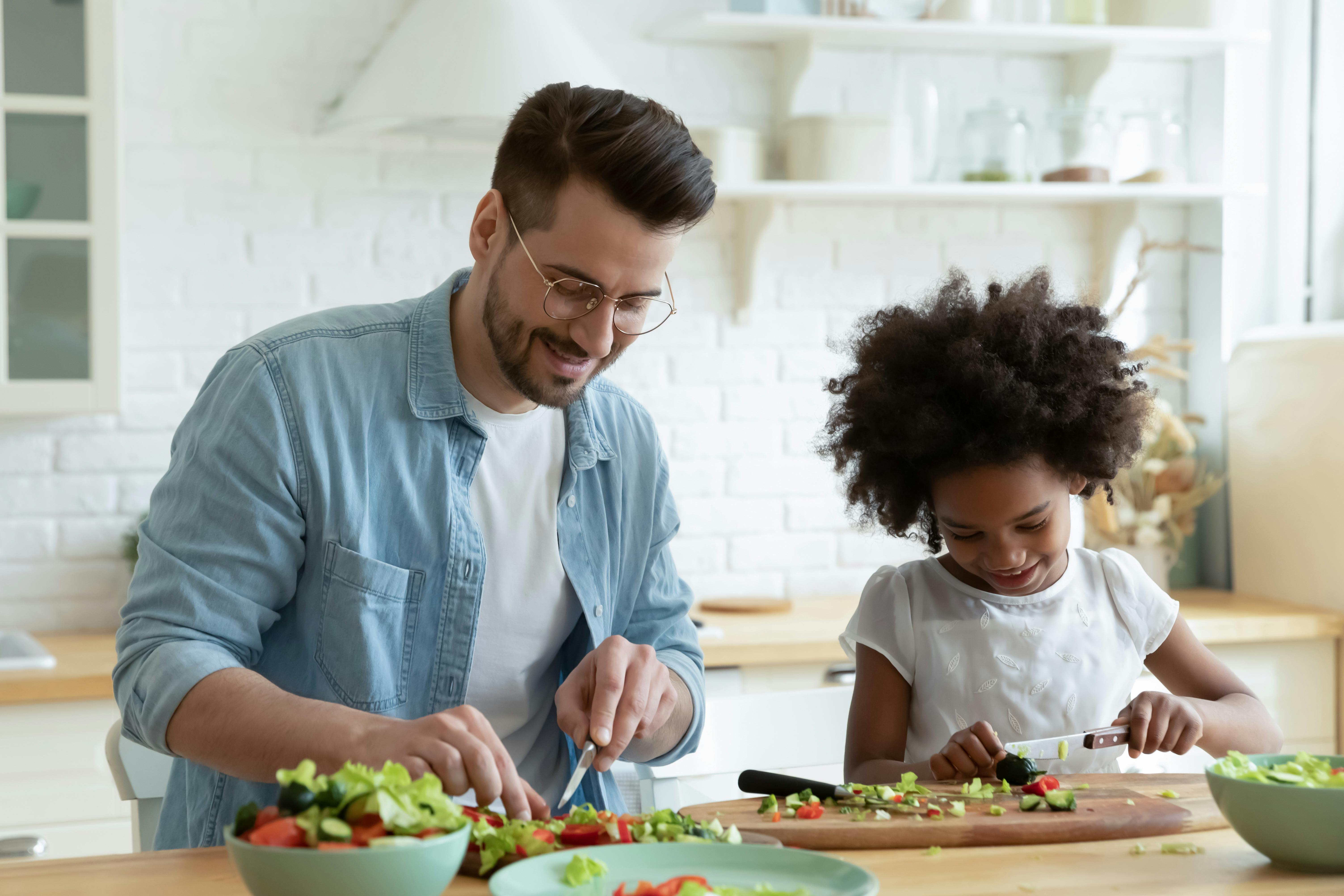 Un homme et une petite fille coupent des légumes dans une cuisine moderne.