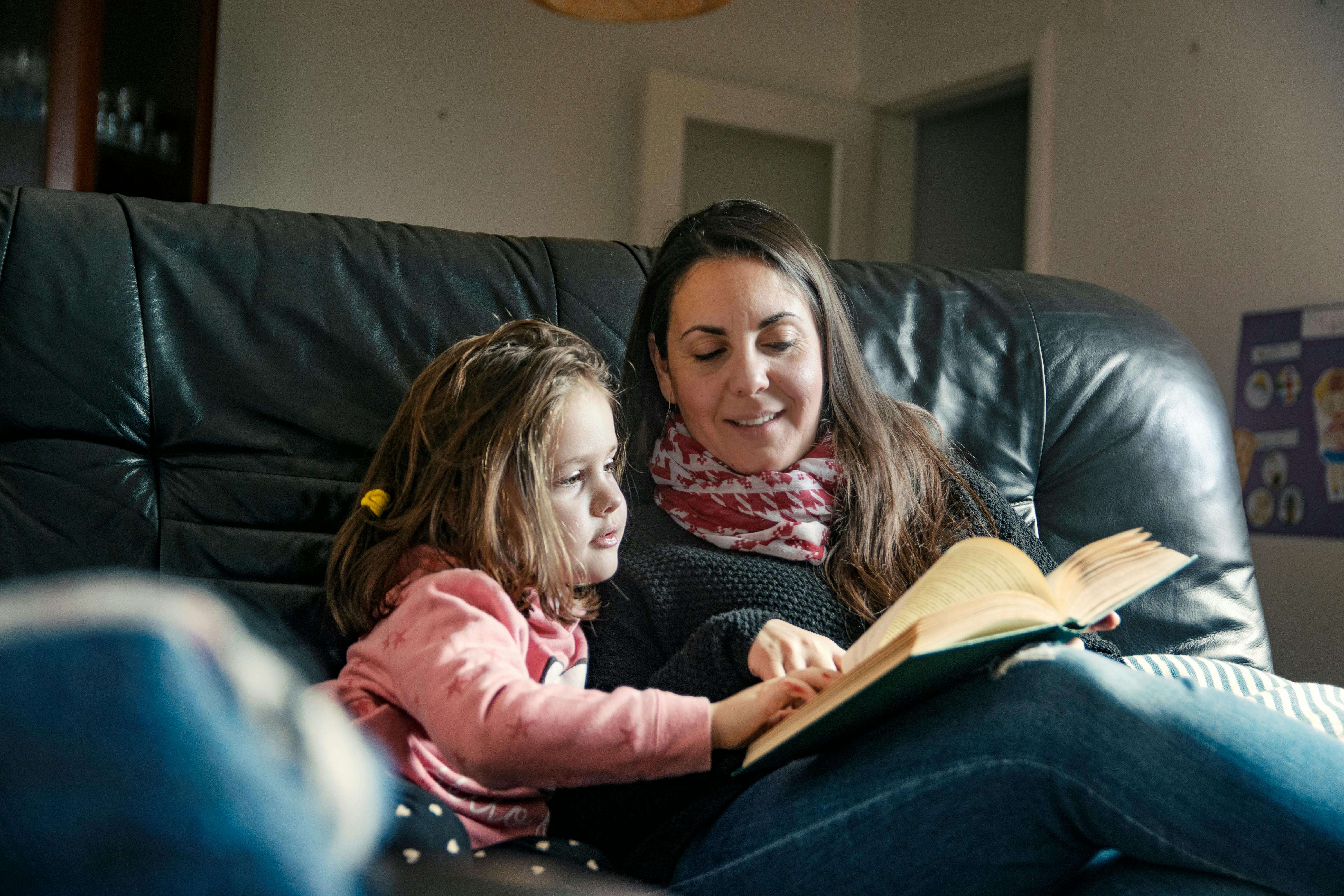Une baby-sitter lit un livre à sa fille sur un canapé en cuir dans leur salon.