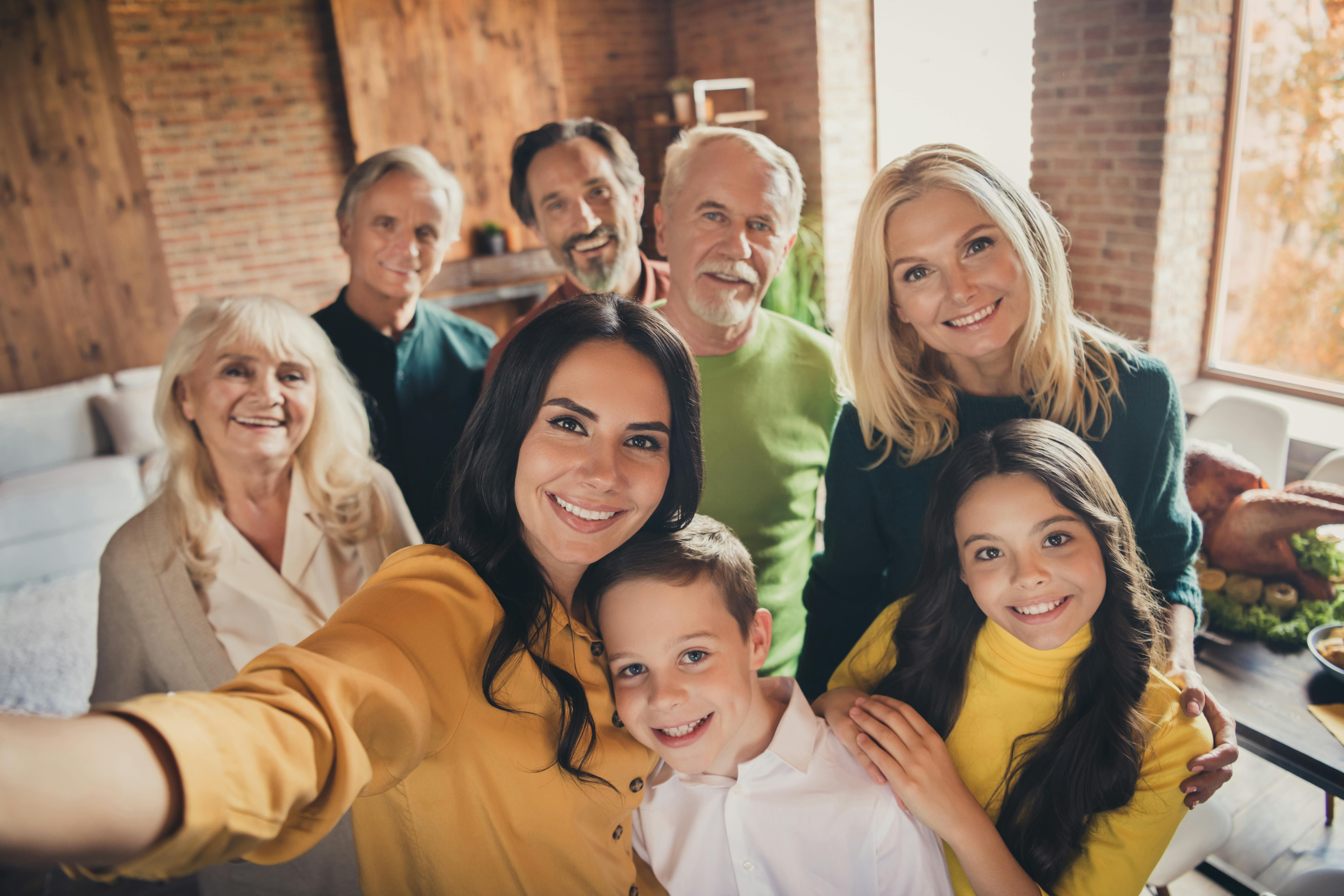 Une famille multigénérationnelle prend un selfie lors d'un repas festif à l'intérieur.