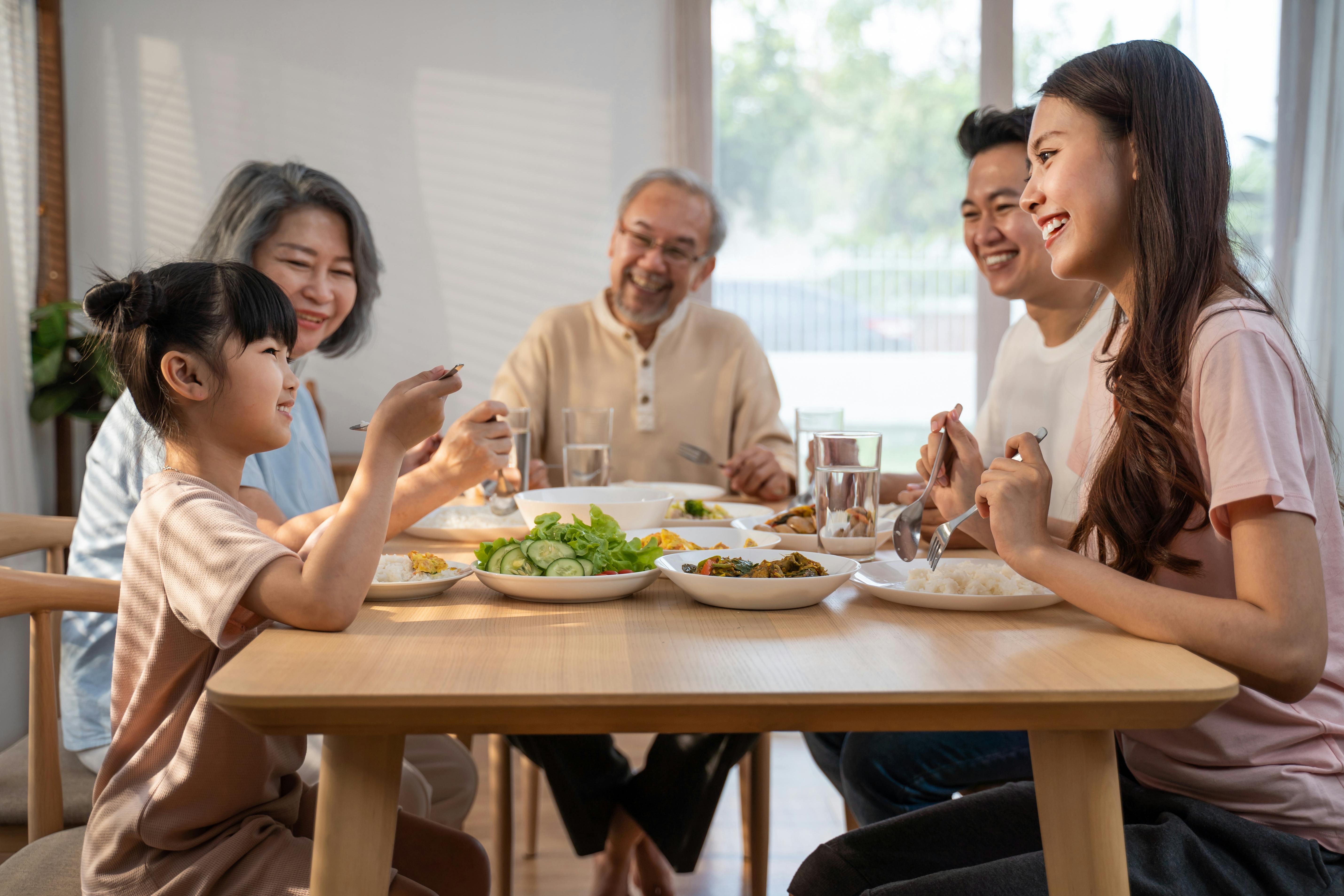 Une famille asiatique partage un repas autour d'une table dans une maison lumineuse.
