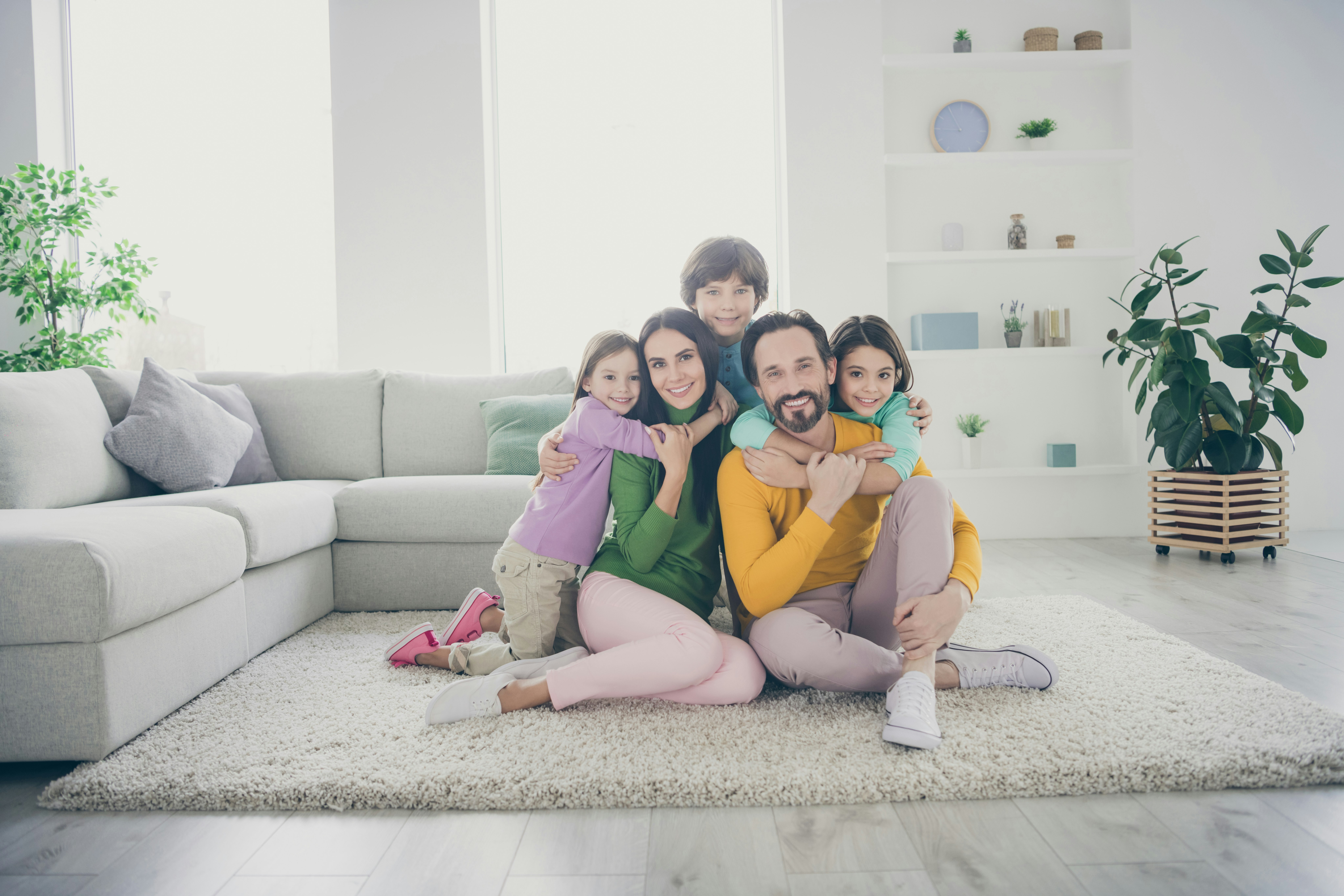 Une famille colorée sourit sur un tapis dans un salon spacieux.