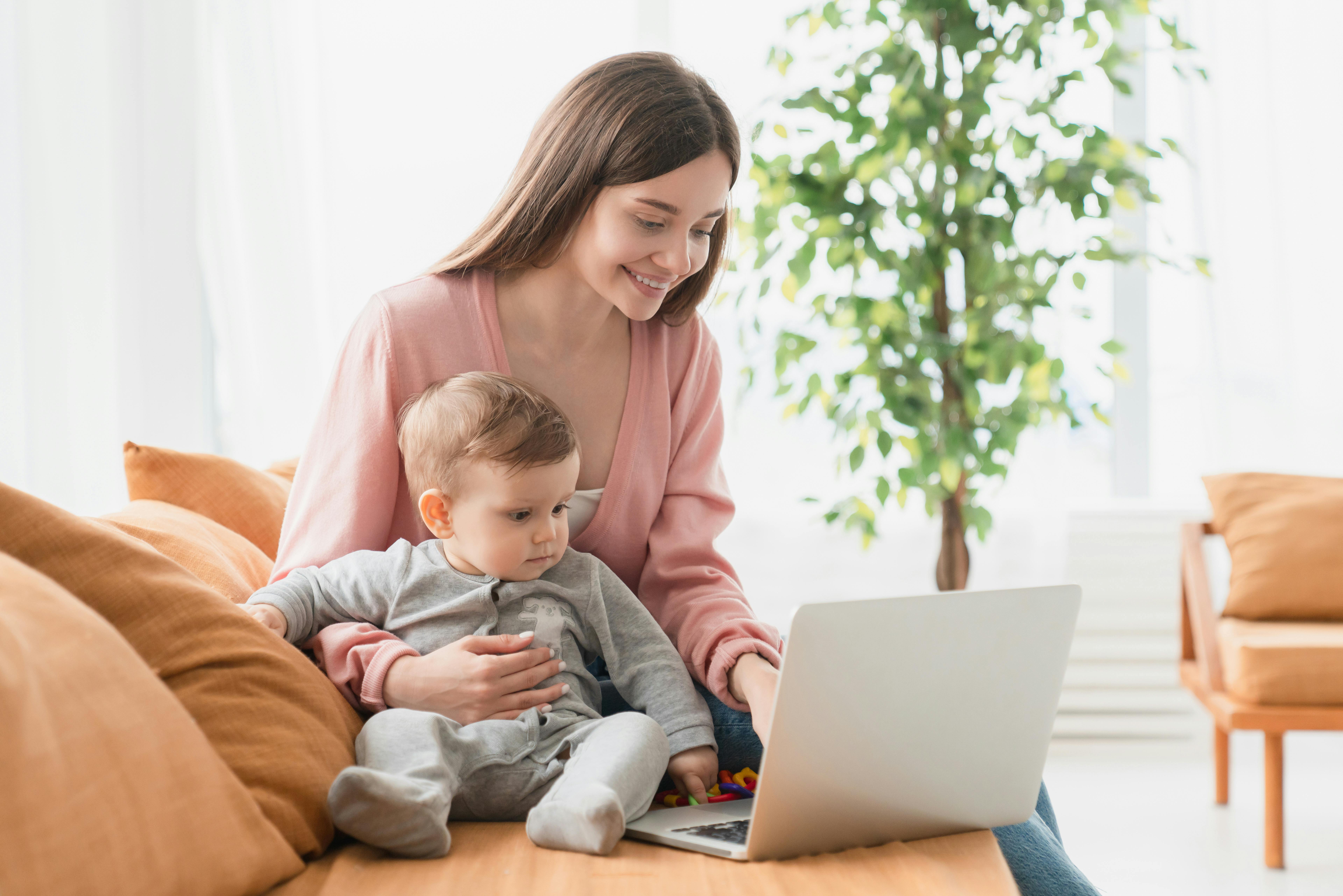 Une mère souriante avec son bébé sur ses genoux utilisant un ordinateur portable.
