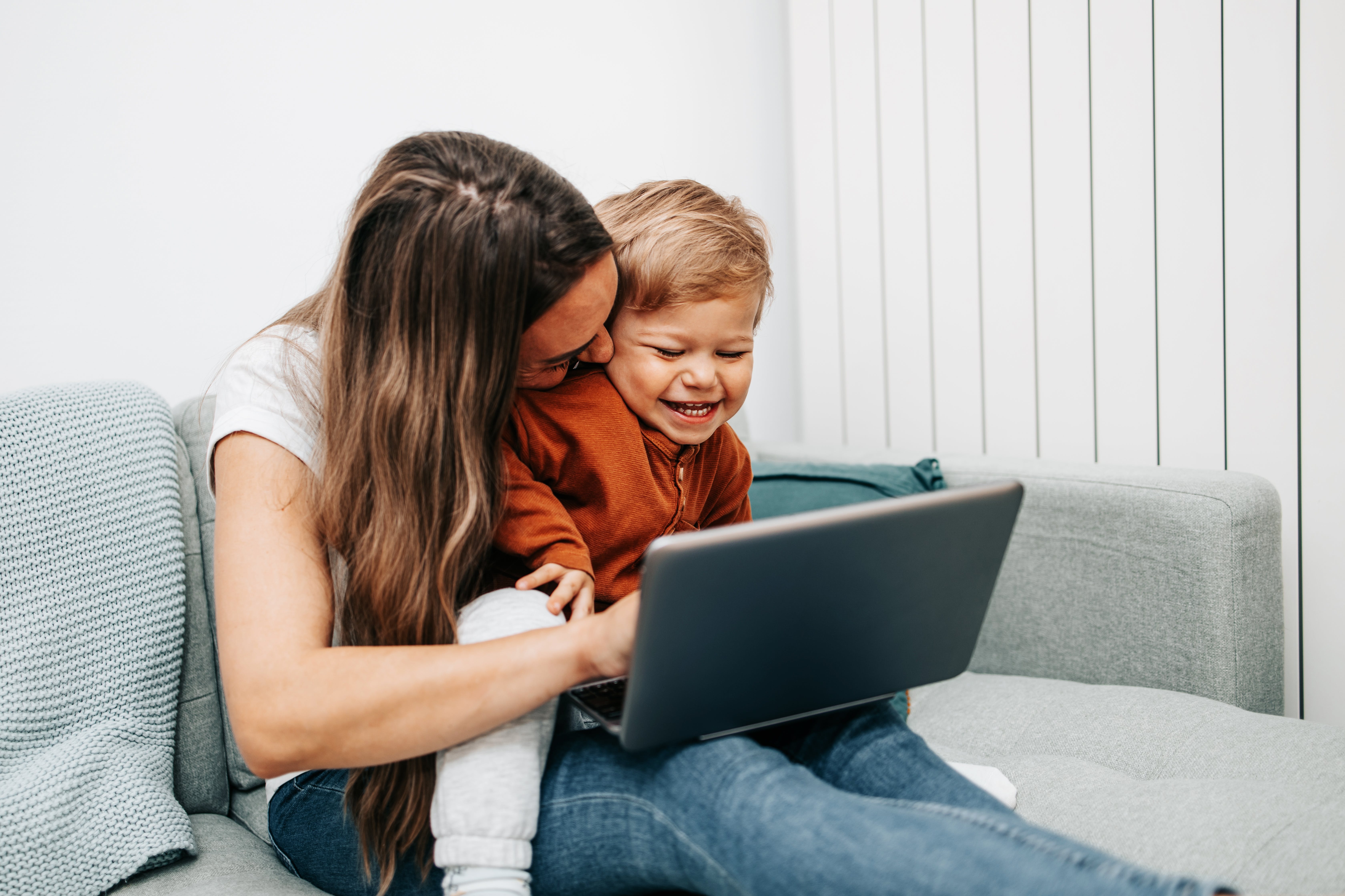 Une femme utilise un ordinateur portable avec un enfant souriant assis sur ses genoux.