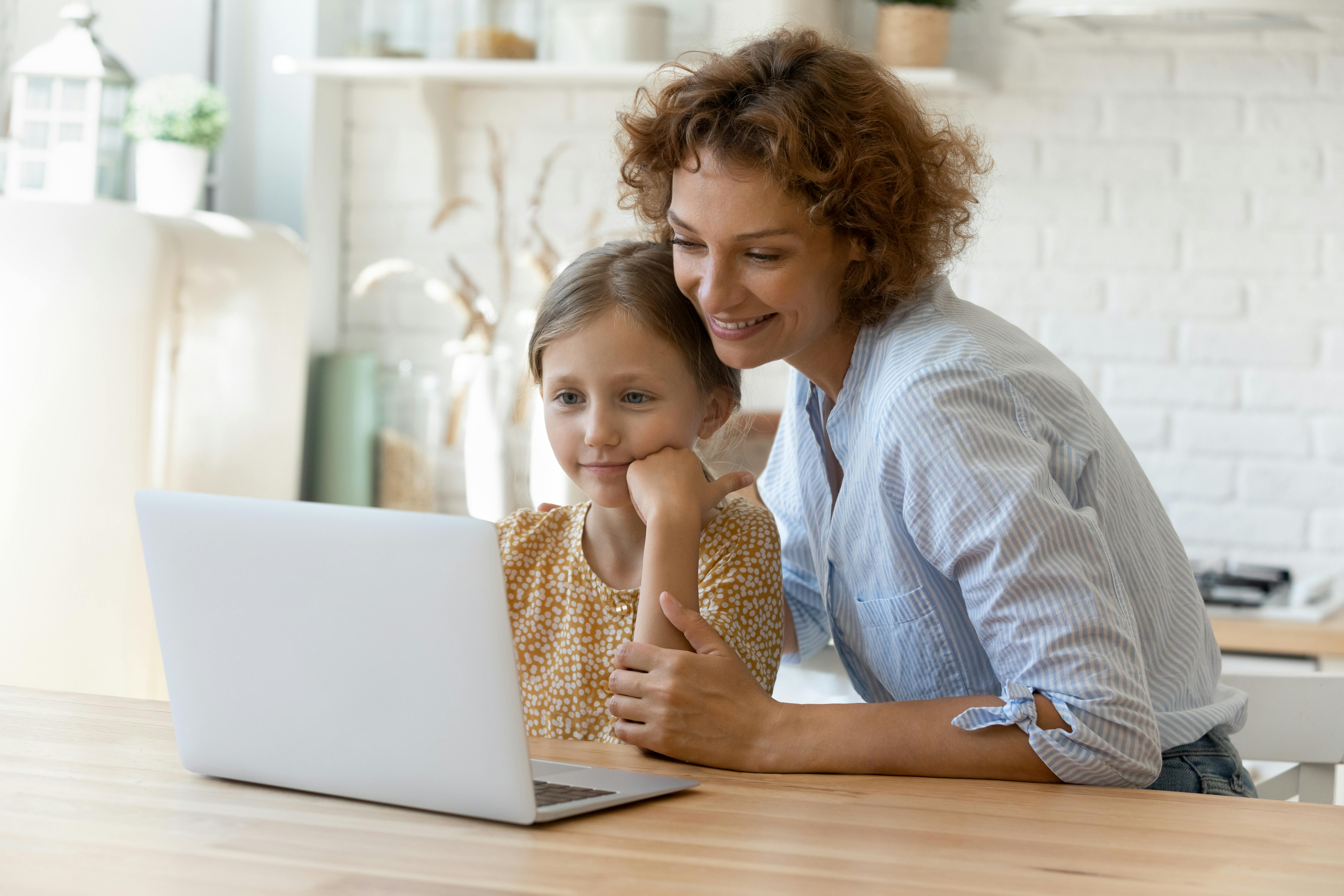 Une femme et une petite fille sourient en regardant un ordinateur portable ensemble.