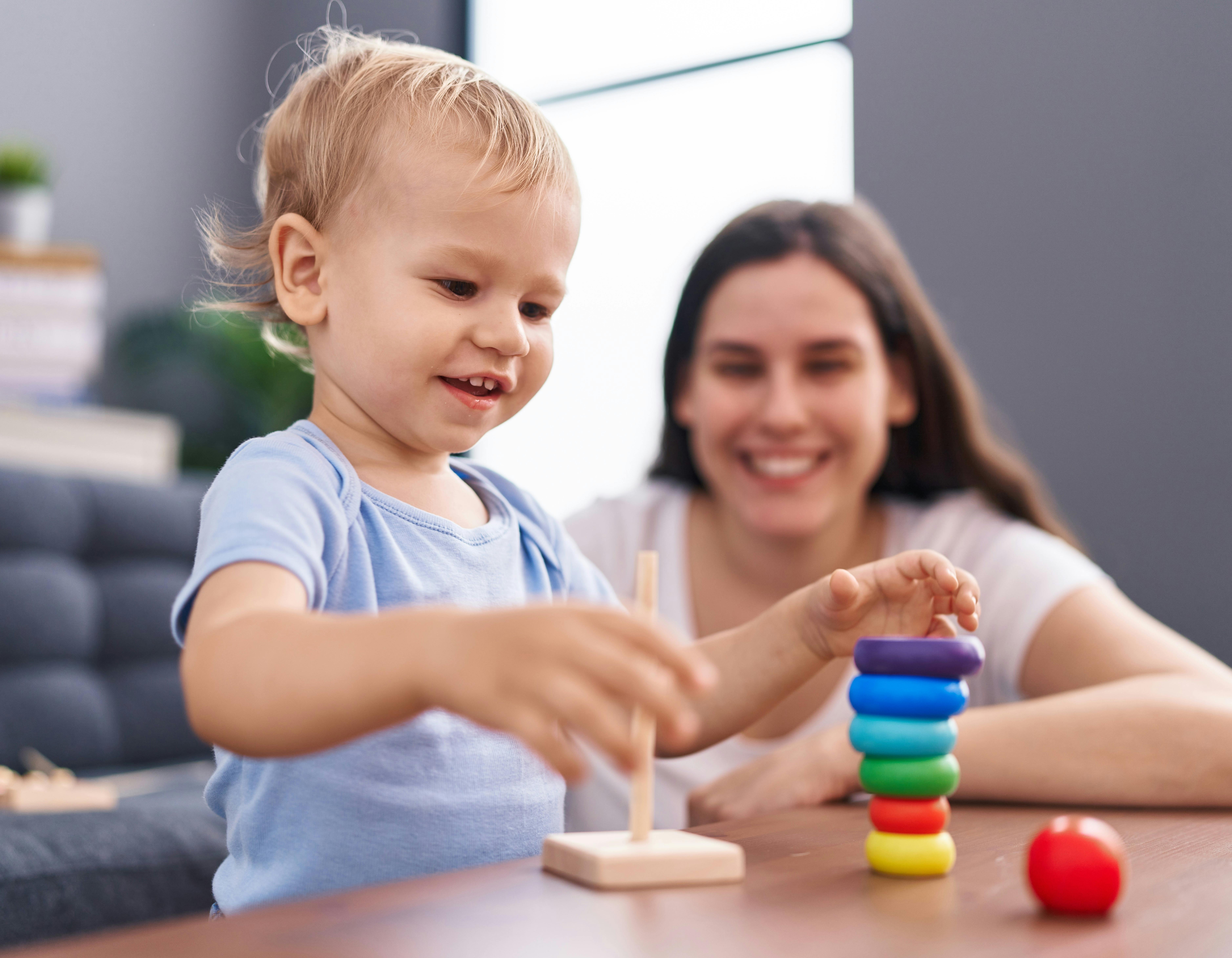 Une femme souriante regarde un enfant jouer avec des anneaux colorés.