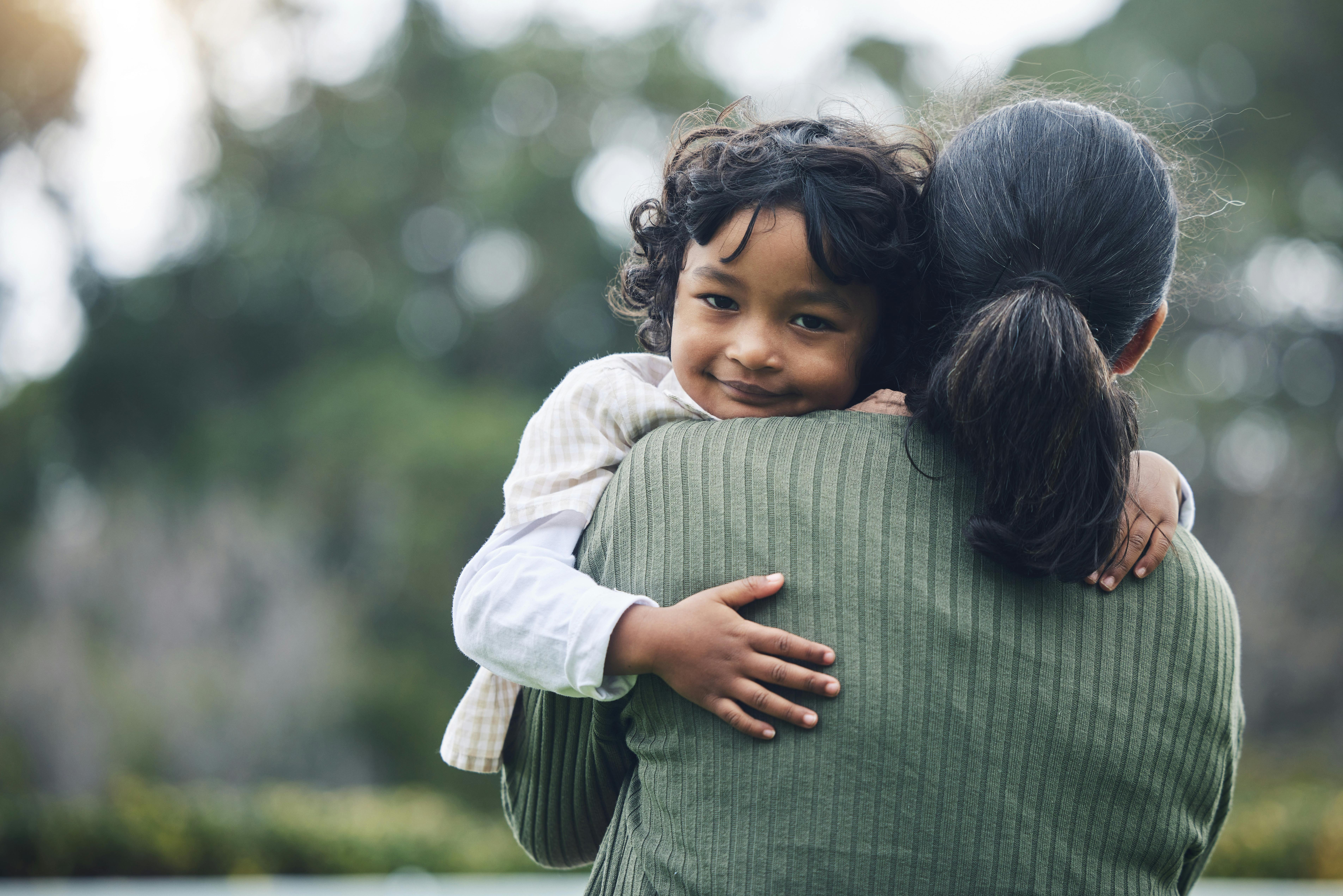 Enfant souriant se faisant câliner par un adulte.
