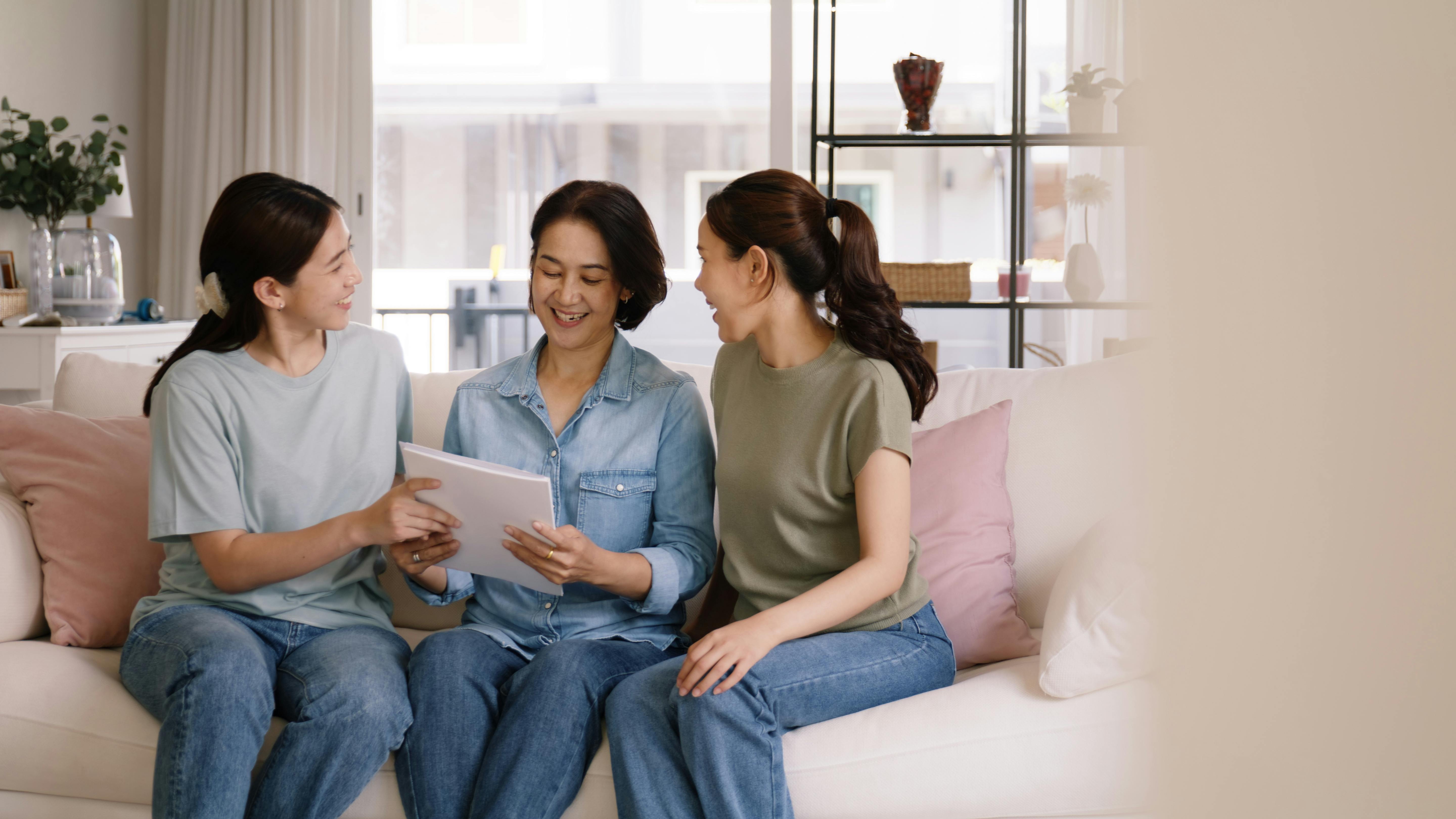 Trois femmes souriantes assises sur un canapé en train de regarder une tablette.