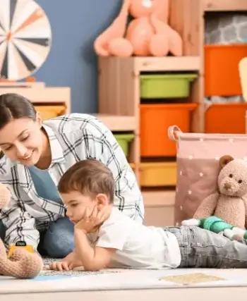 Une baby-sitter jouant avec un petit garçon dans une pièce remplie de jouets.
