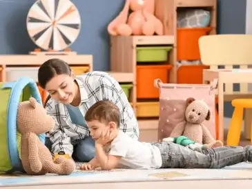 Une baby-sitter jouant avec un petit garçon dans une pièce remplie de jouets.
